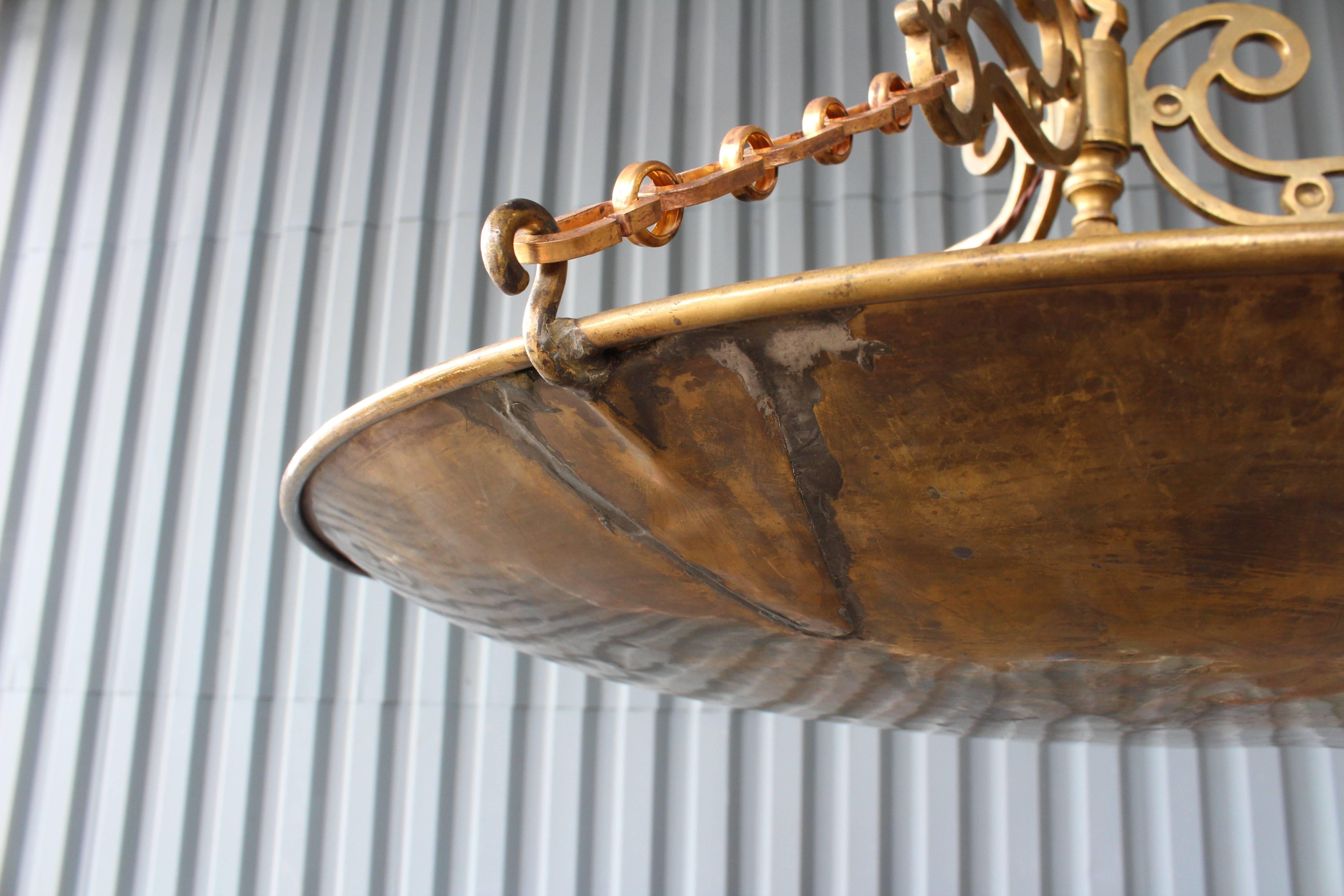 A beautiful solid brass pendant light custom-made from a vintage brass saucer. This hanging light has been recently wired with four lights. Brass retains original aged patina.