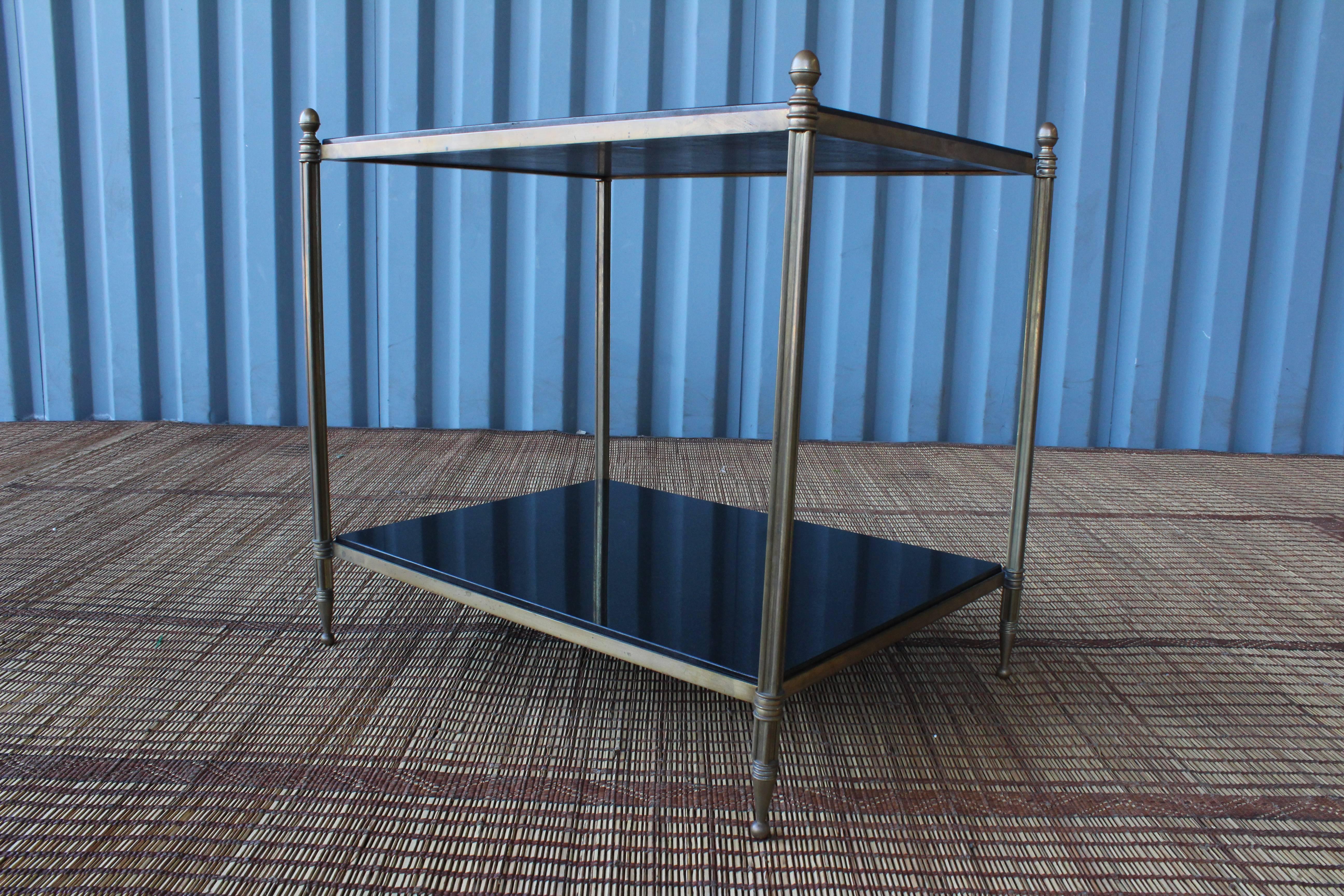 Solid brass two-tiered side table with black granite tops, France, 1950s. Excellent condition with age appropriate patina to the brass.