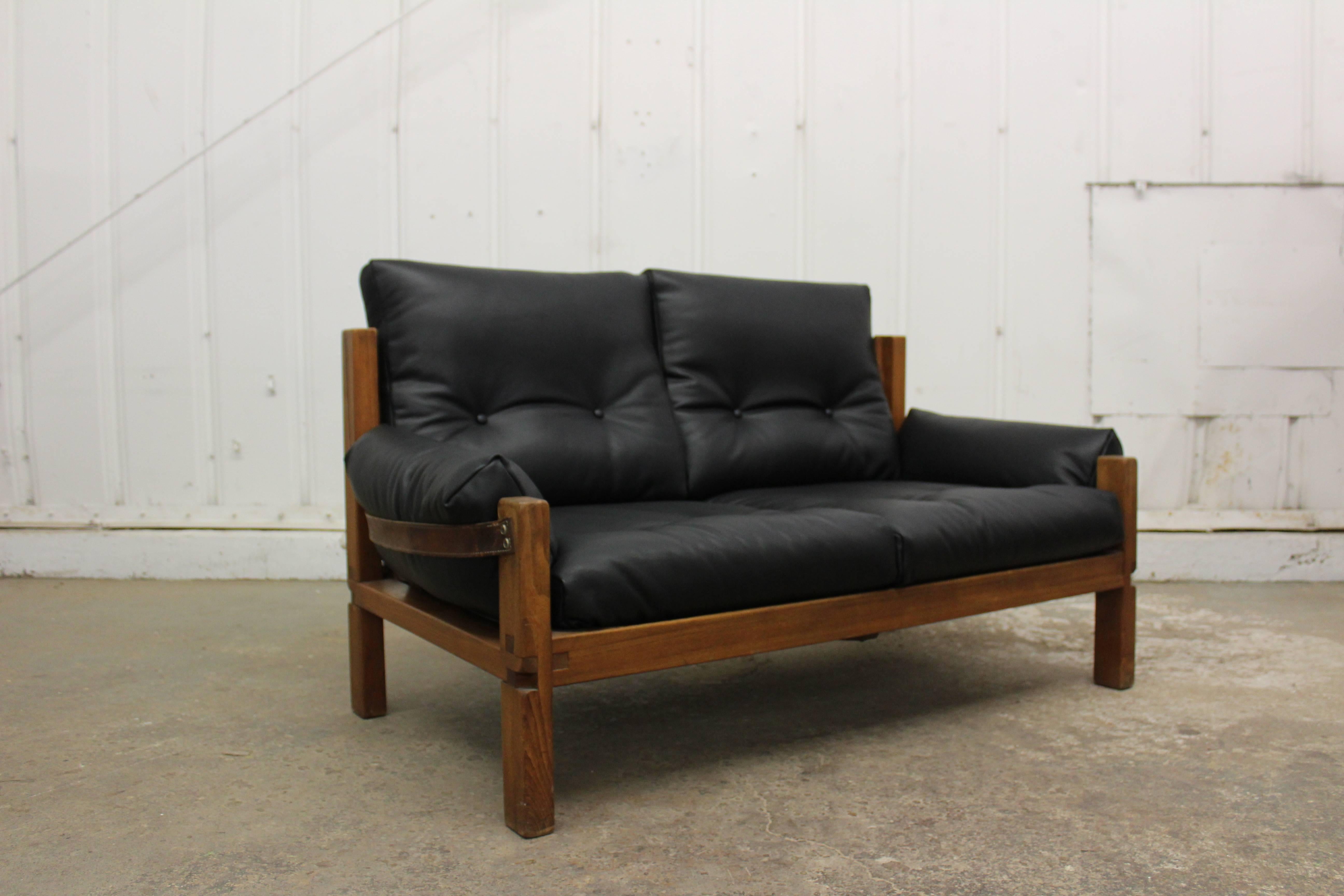 Loveseat designed by Pierre Chapo, France, 1950s. Frame constructed in solid elm and new black leather cushions with original leather straps and hardware.