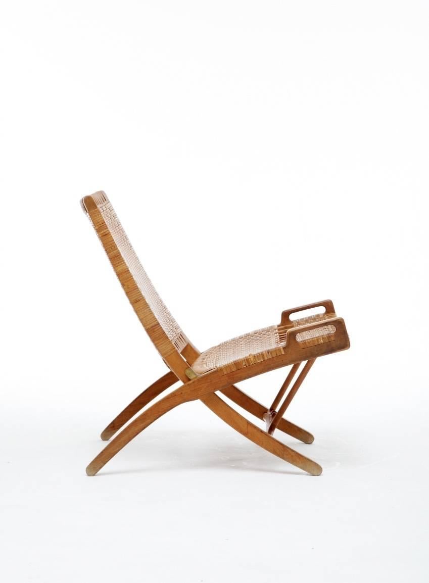 Folding chair, designed by Hans J. Wegner, 1950s, Denmark.  Designed 1949, made and burn marked by cabinetmaker Johannes Hansen, model JH-512.
A bench-made oak folding chair with caned seat and backrest. 
The chair is designed to be hung on the wall