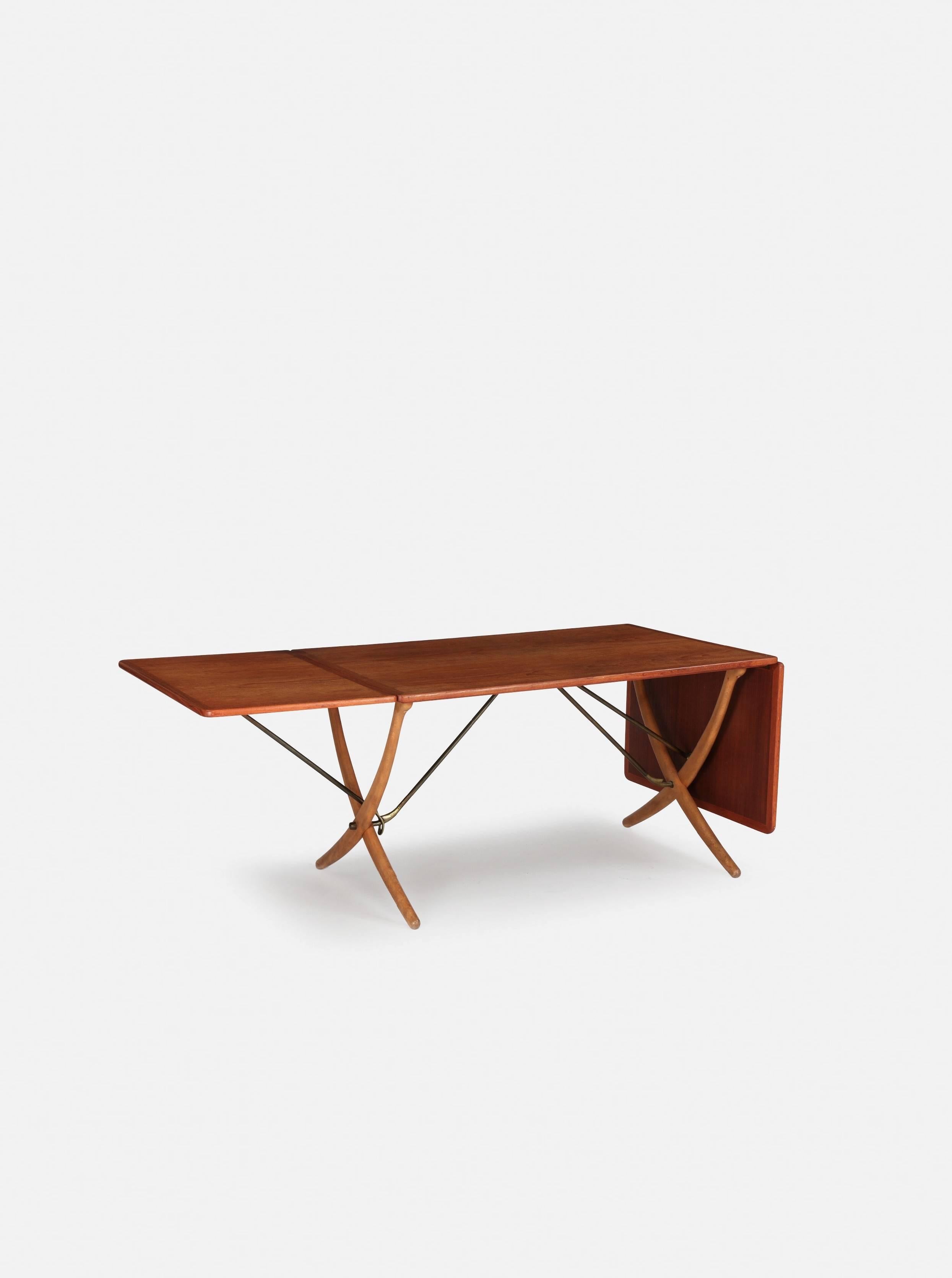 Hans Wegner AT 304 dining table, made by Andreas Tuck in Denmark, 1960s.
Teak with beech cross legs and brass bars. Two flip up / extendable leaves. Length is 128cm unextended, 178cm with one leaf up and 238 cm with both leaves extended. Width 86