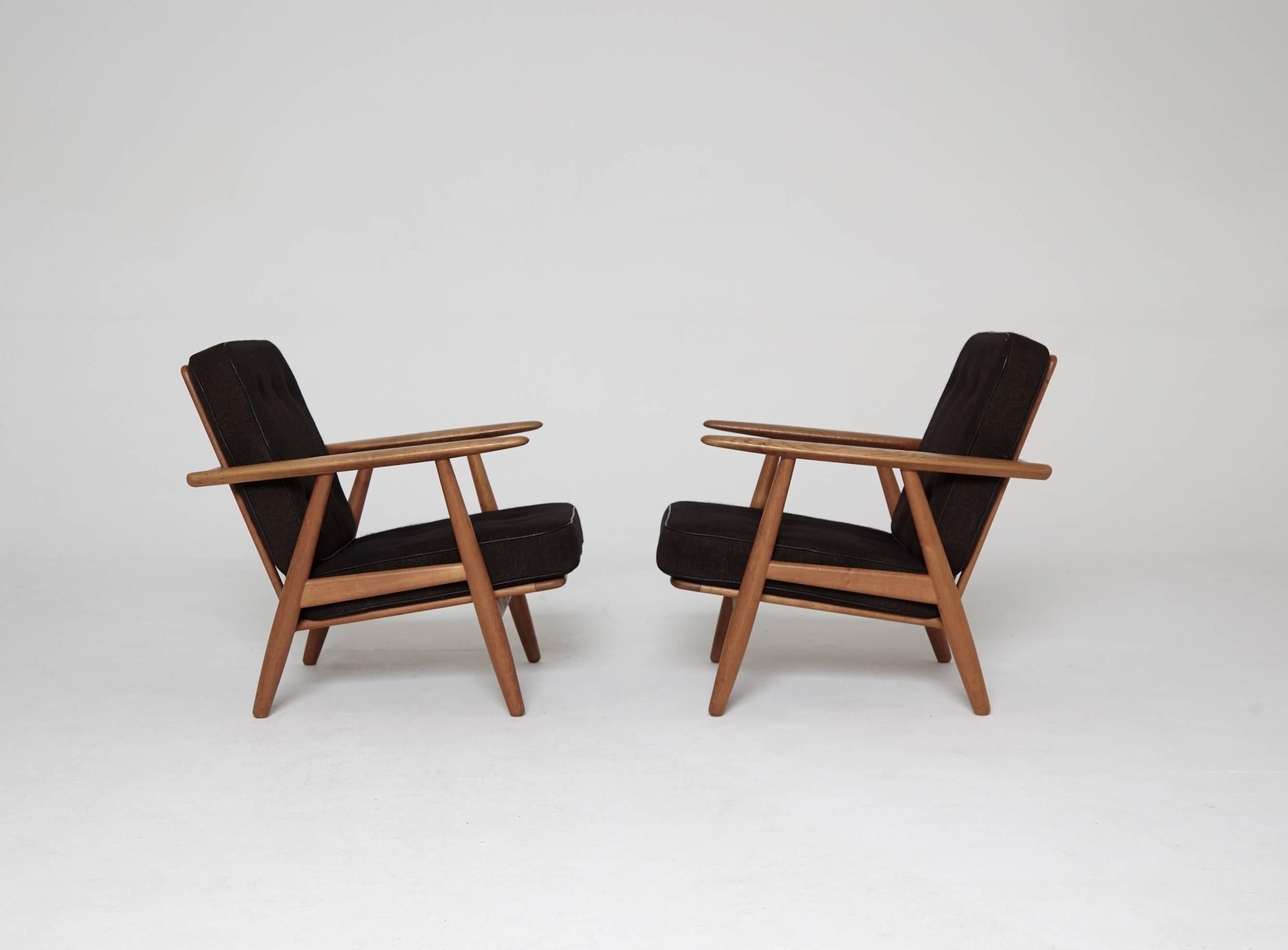 A pair of oak GE-240 Cigar lounge chairs designed by Hans J. Wegner and produced by GETAMA, Denmark. The oak frames are in excellent vintage condition with only very minor signs of age and use.  Original sprung cushions upholstered in original black