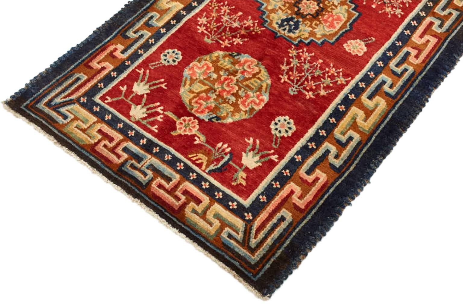 Handwoven from wool in Nepal, this vintage rug features a trio of mandalas set within a deep crimson field and accented by stylized floral motifs. A border of 'endless knots', symbols thought to have powers that bring happiness, long life, love, and
