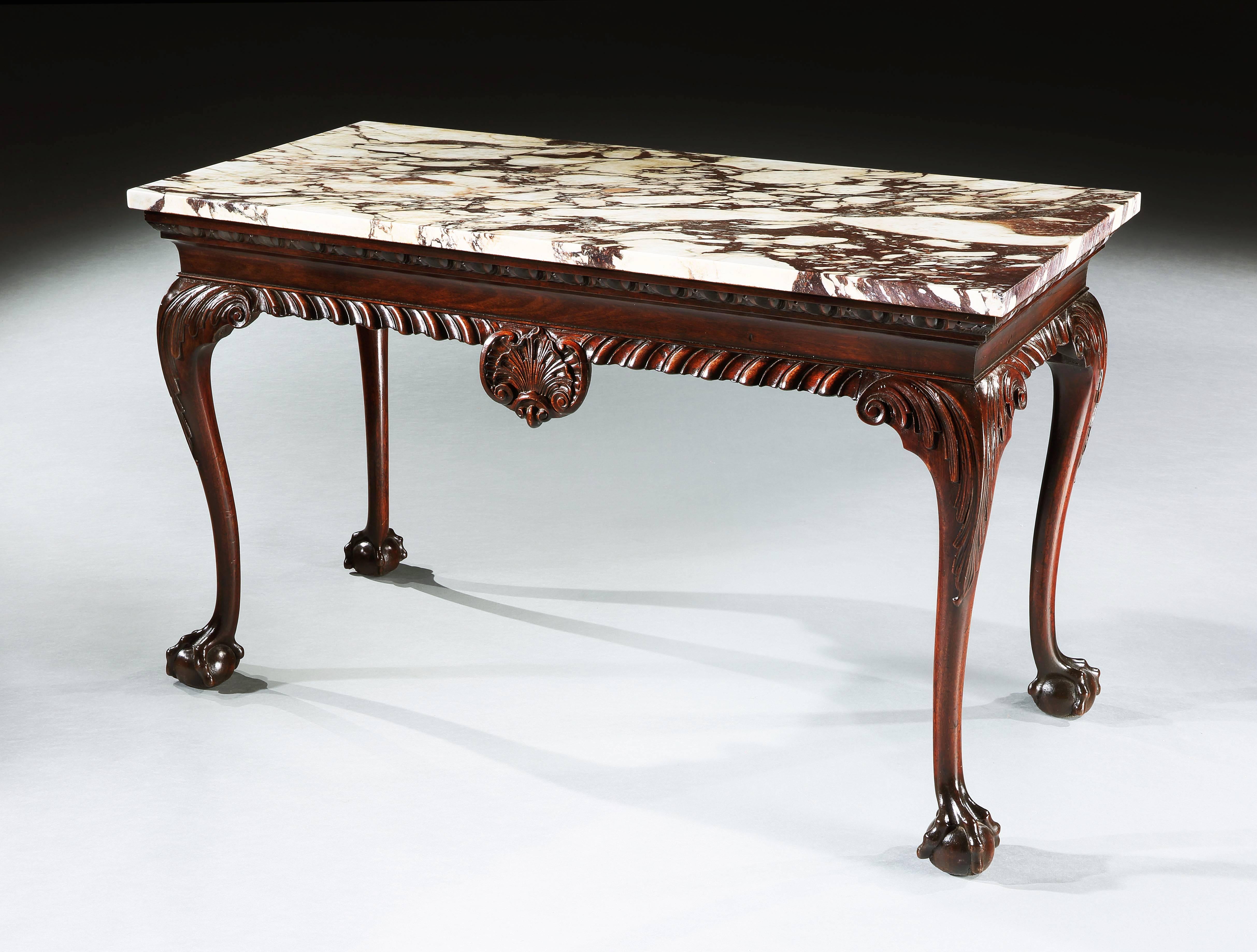 A George II side table in mahogany with a Carrara Brescia Violetta marble top above an egg and dart moulding. The frieze with a carved gadrooned edge centered by a shell and standing on cabriole legs carved with acanthus, and terminating in ball and
