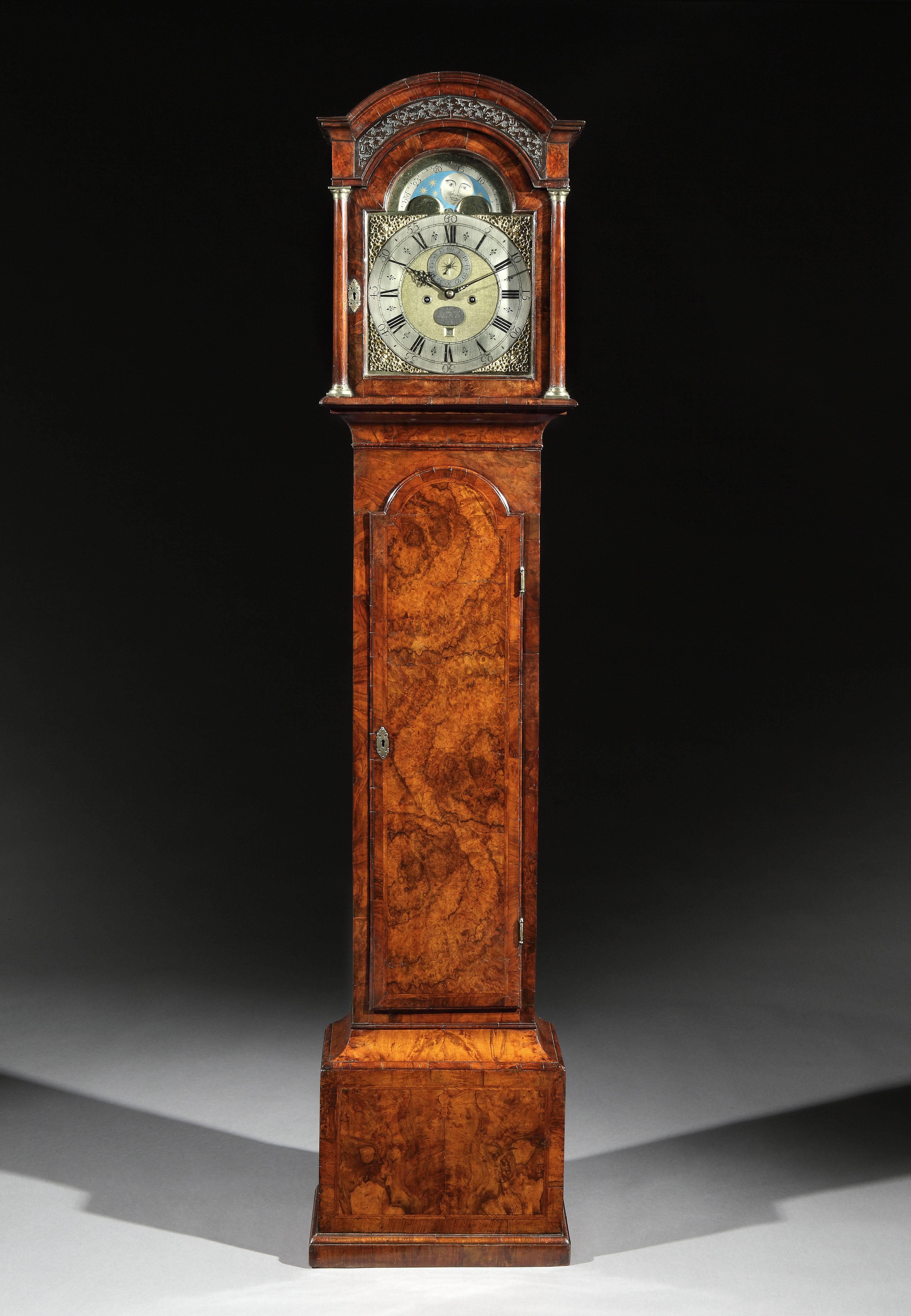 An early George II figured walnut long case clock of elegant proportions, inlaid and cross-banded throughout. The slim case standing on a moulded plinth, the arched hood with a panel of fretwork flanked by tapering columns. The movement with an