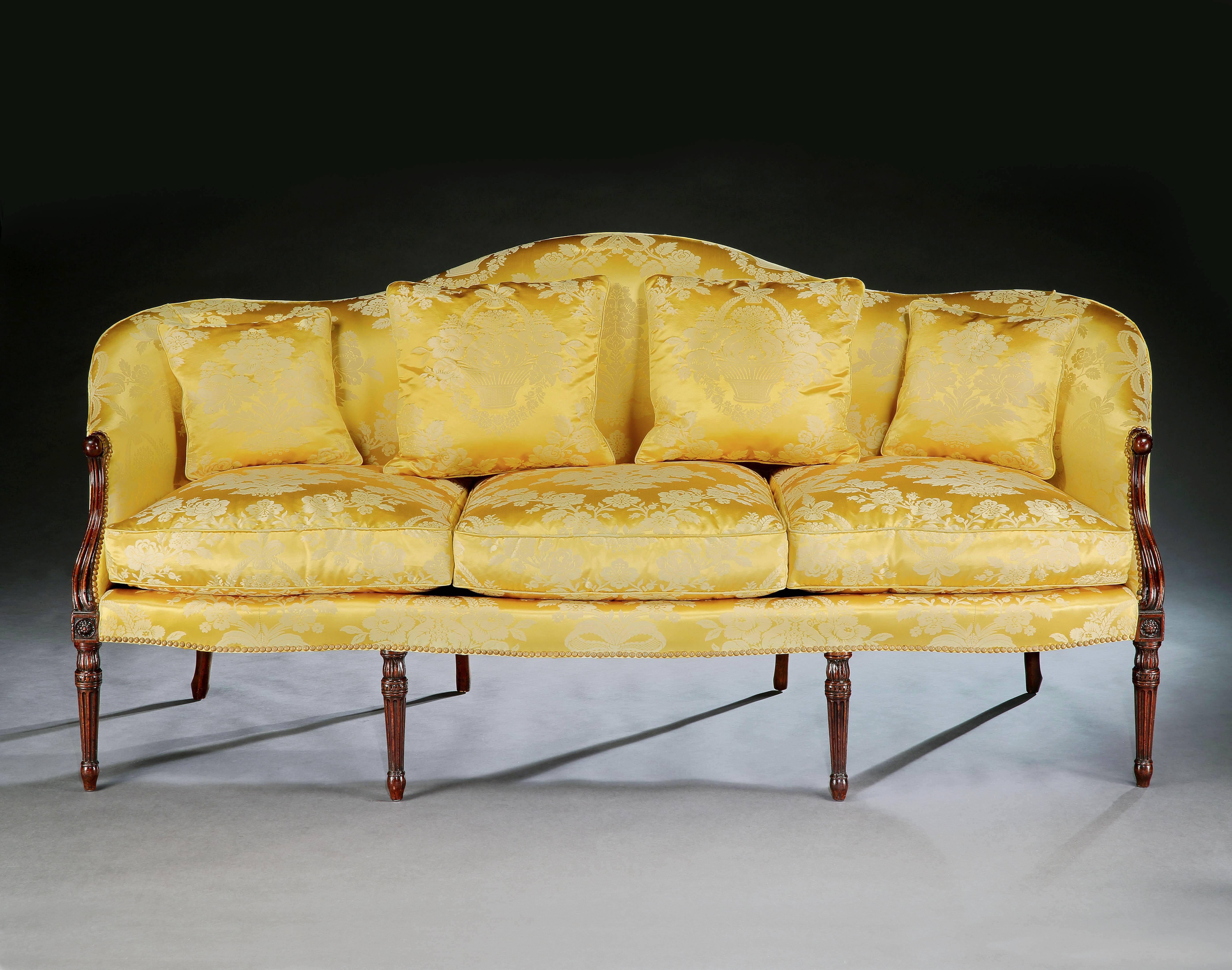 A particularly elegant and finely carved George III three-seat mahogany settee, the serpentine shaped back central to carved end supports, terminating in carved and fluted legs headed by paterae. The settee and cushions covered in a yellow and gold