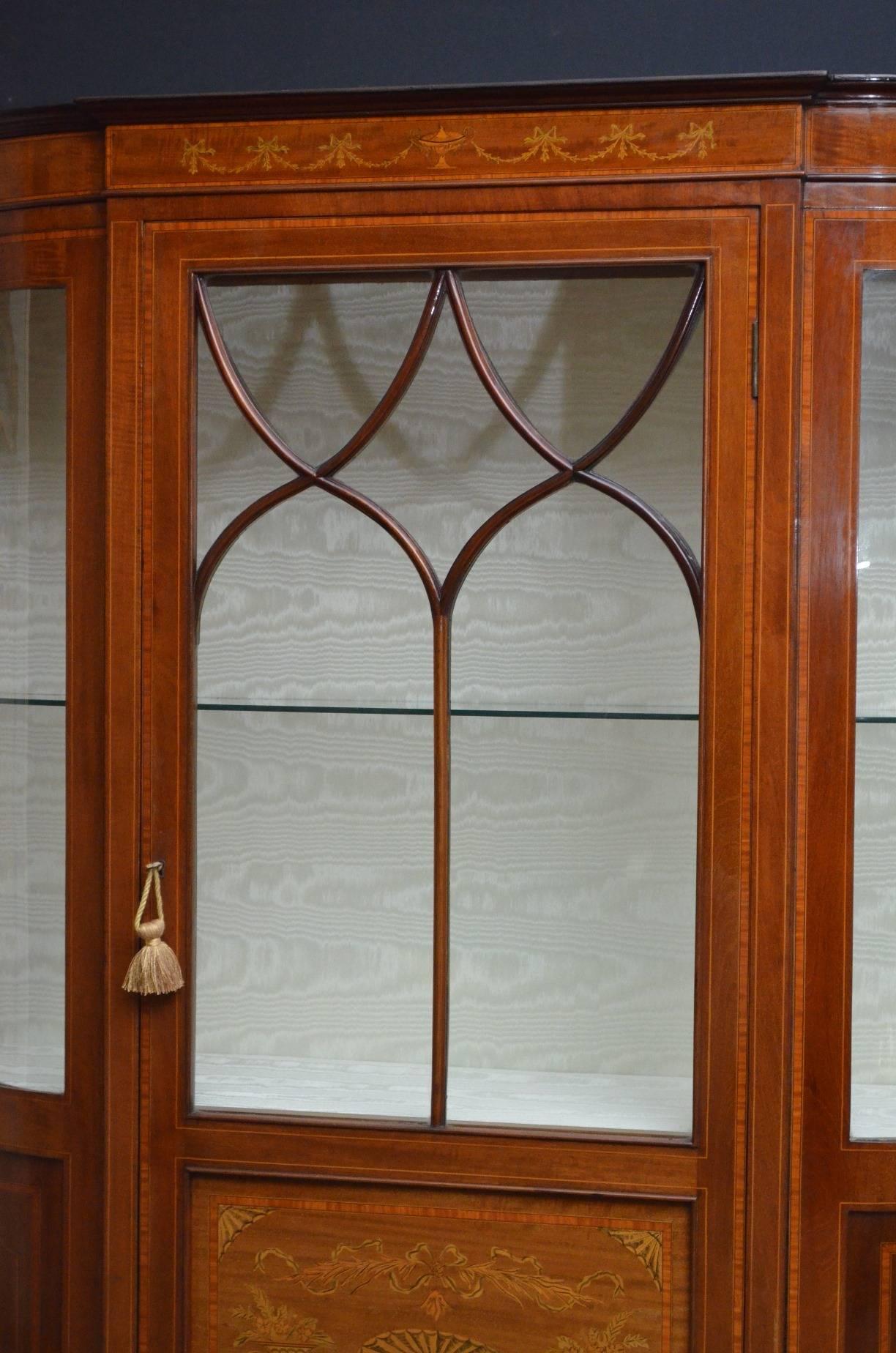 Sn3792 stunning Edwardian, mahogany and inlaid display cabinet, having moulded cornice above swags and ribbon ties inlaid frieze, astragal glazed door with marquetry panel below enclosing two shelves, all flanked by glazed, bowed sides with