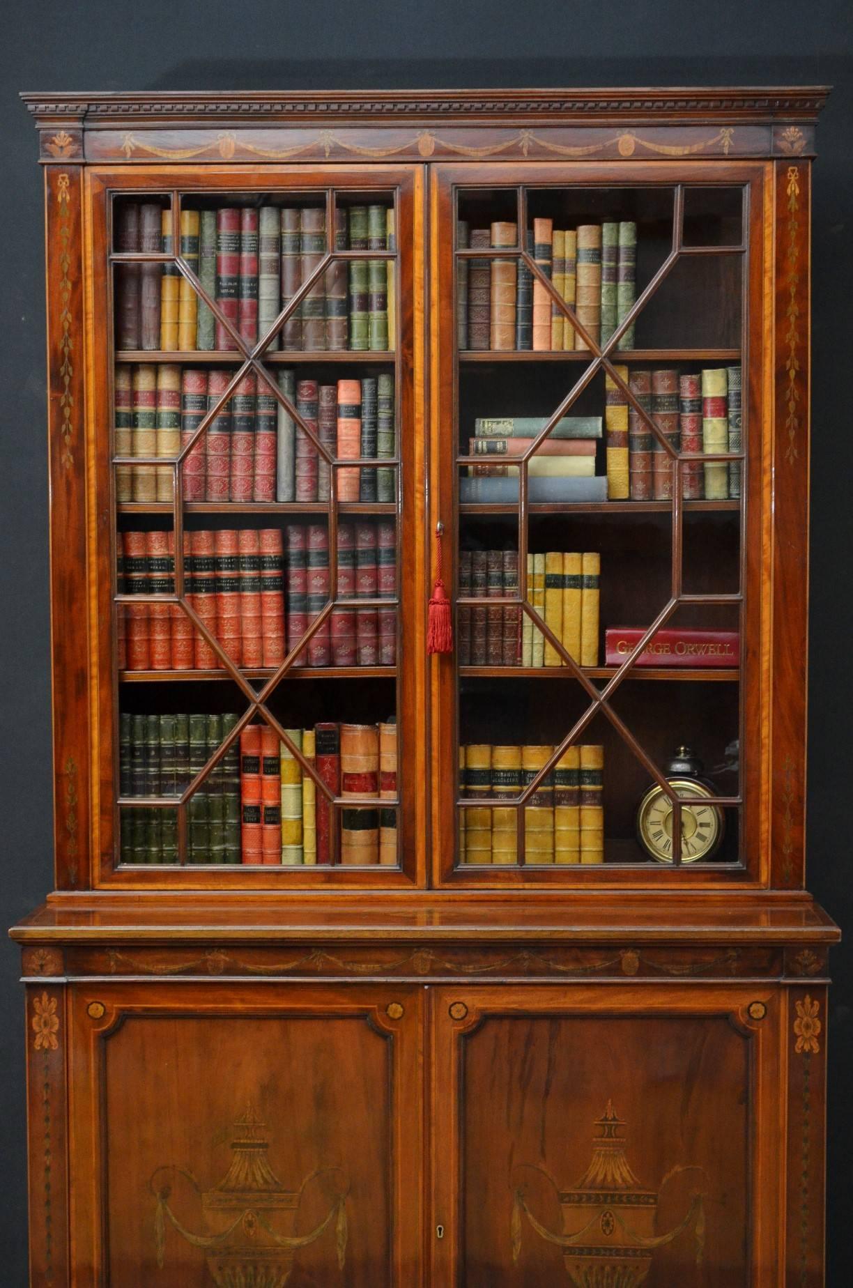Sn4043 An attractive Edwardian bookcase in mahogany, having cavetto cornice with dentil carving and finely inlaid frieze above astragal glazed doors enclosing three height adjustable shelves, all flanked by floral inlays, base having pair of