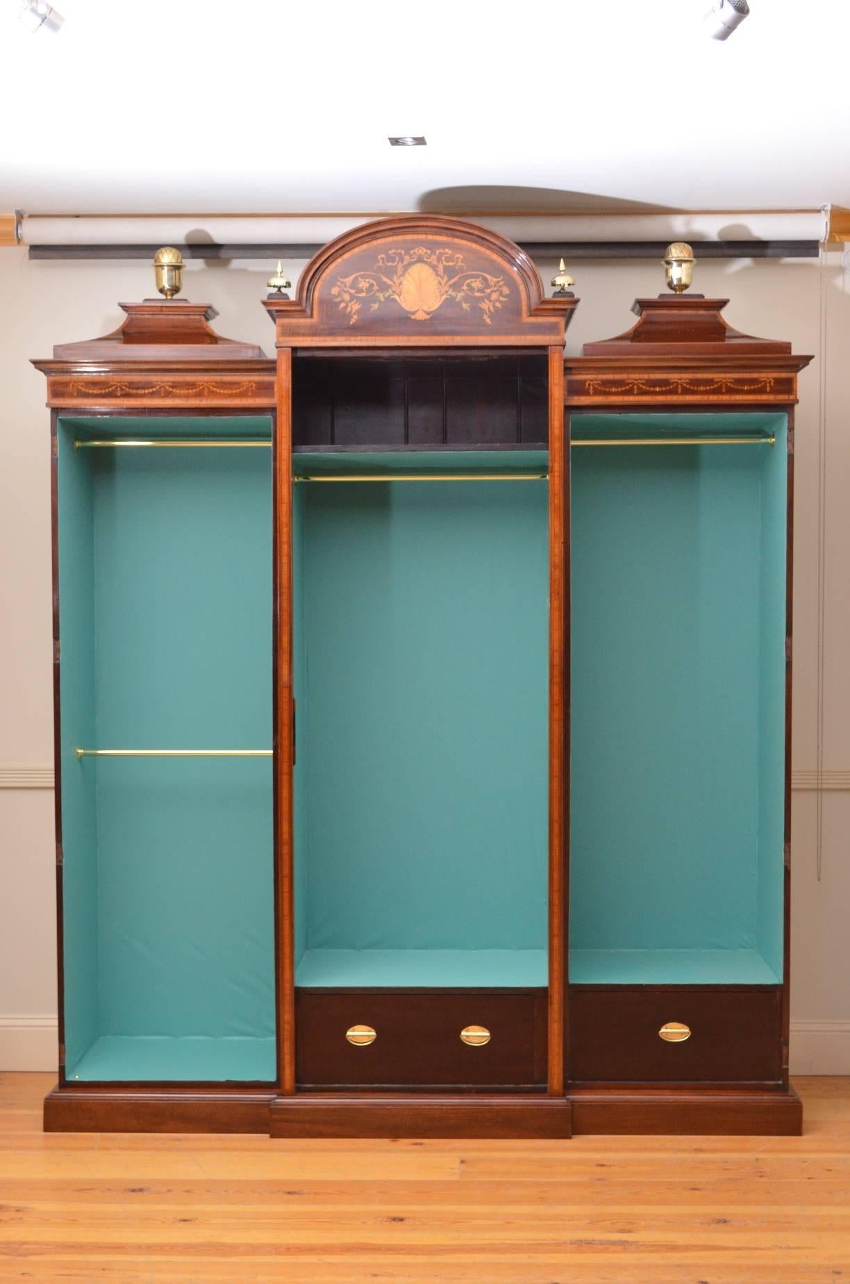 Sn4083, striking waring and gillow mahogany three-door wardrobe, having mirrored centre door with finely inlaid arched pediment flanked by small brass finials all enclosing shelf, hanging space and a drawer and flanked by panelled and inlaid