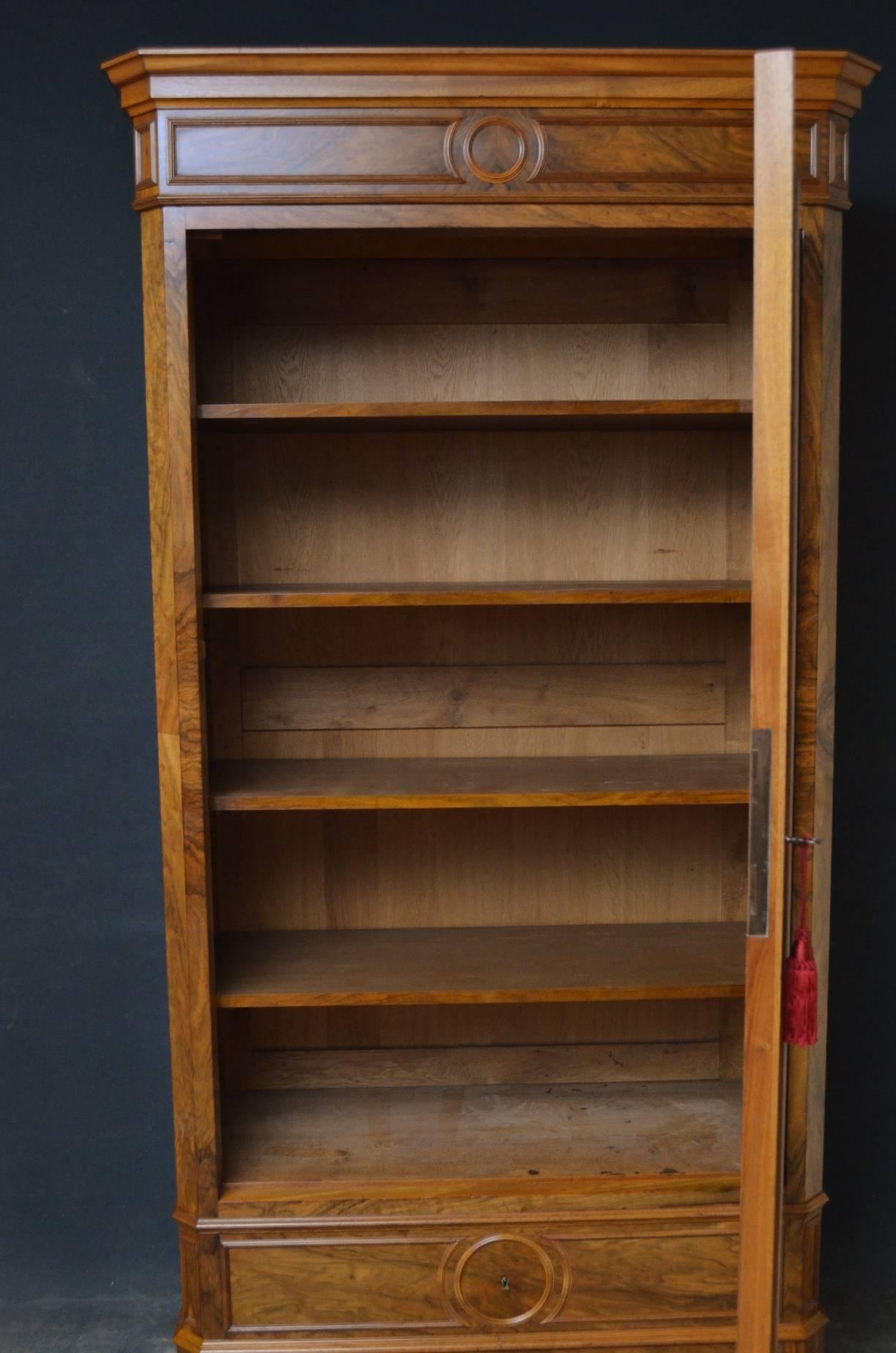 Sn4079 Very attractive figured walnut bookcase, having out swept, moulded cornice and single glazed door enclosing four height adjustable shelves above two oak lined drawer, all standing on plinth base and pad feet. This fine bookcase is in