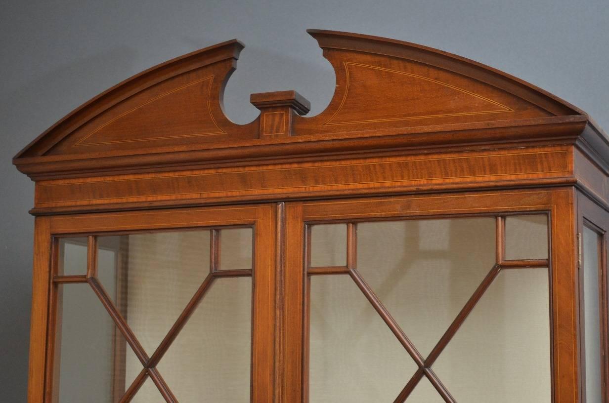 Sn3189, fine quality Edwardian, mahogany display cabinet or china cabinet, having string inlaid architectural pediment with crossbanded frieze and a pair of astragal glazed doors enclosing two relined shelves above bowed projecting base with two