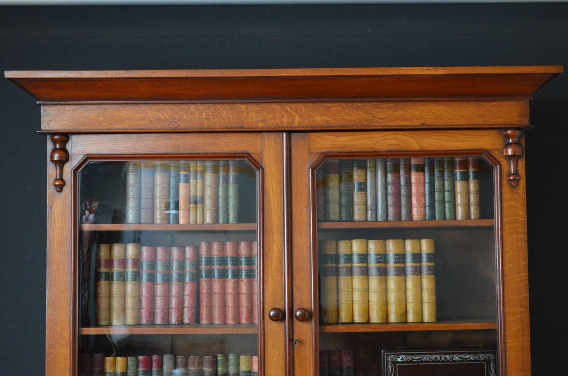 Sn2199, a Victorian oak and mahogany country bookcase, having moulded cornice, three shelves enclosed by pair of glazed door flanked by drop carvings. Base having two shaped drawers above a pair of panelled cupboard door with carvings to sides, all