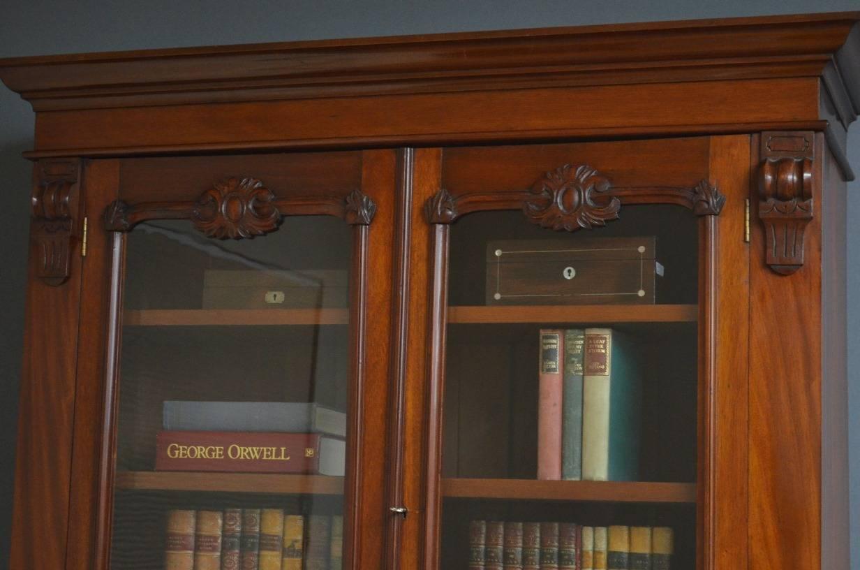 Sn3218 Victorian bookcase in mahogany with moulded and out swept cornice, a pair of glazed doors enclosing three height adjustable shelves and two practical drawers, all flanked by drop carvings, the base having two fielded drawers and a pair of