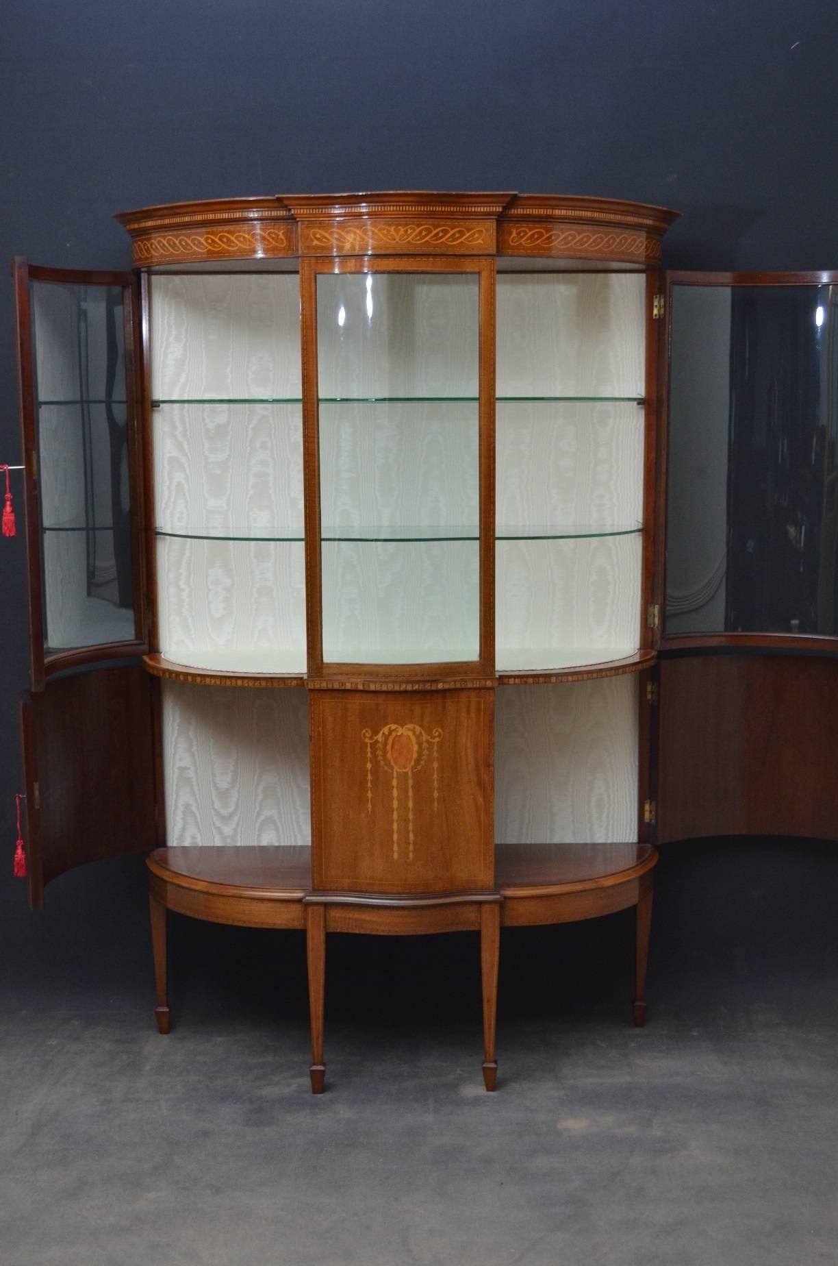 Sn4101 fine example of Edwardian, mahogany china cabinet of serpentine outline, having moulded cornice above finely inlaid frieze above projecting centre section flanked by glazed doors and enclosing relined interior with two glass shelves, the base