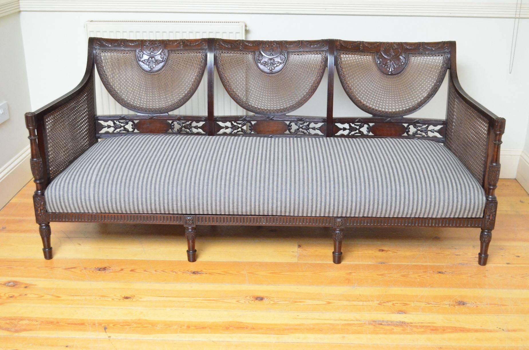 Sn4158 exceptional Edwardian mahogany bergere suite, comprising settee and two armchairs, having swag and bellflowers to top rails, finely carved mid rails, double caned arms and reeded front rails, all standing on turned and carved legs. This fine