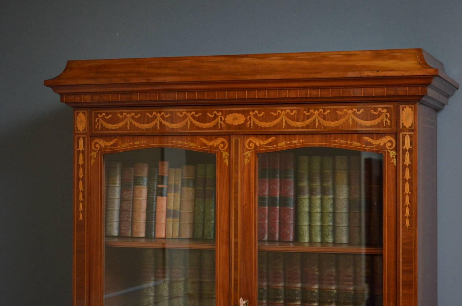 Sn4213 An antique French bookcase in mahogany, having concave cornice above finely inlaid frieze and a pair of glazed doors enclosing height adjustable shelves, fitted with original working lock and key, the base having pair of inlaid and panelled
