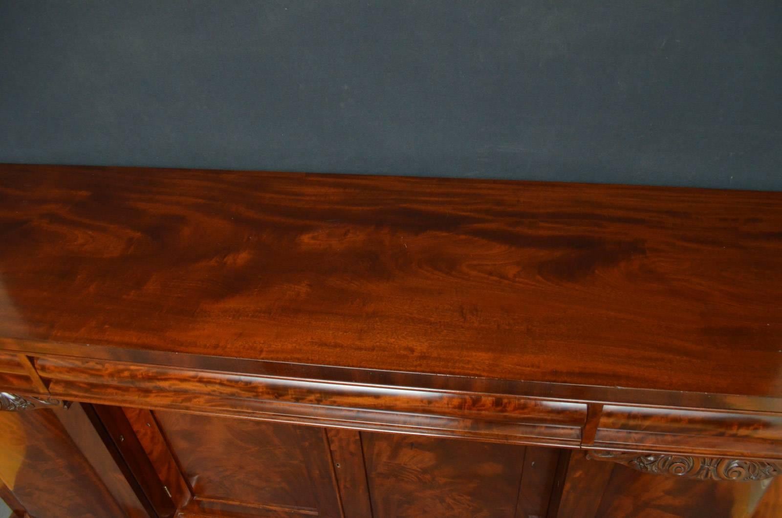 R00 fine quality and very elegant William IV breakfronted sideboard in mahogany, having figured mahogany top above three oak lined cylinder drawers and flamed mahogany cupboard doors enclosing removable shelf, all flanked by further bowed cabinet