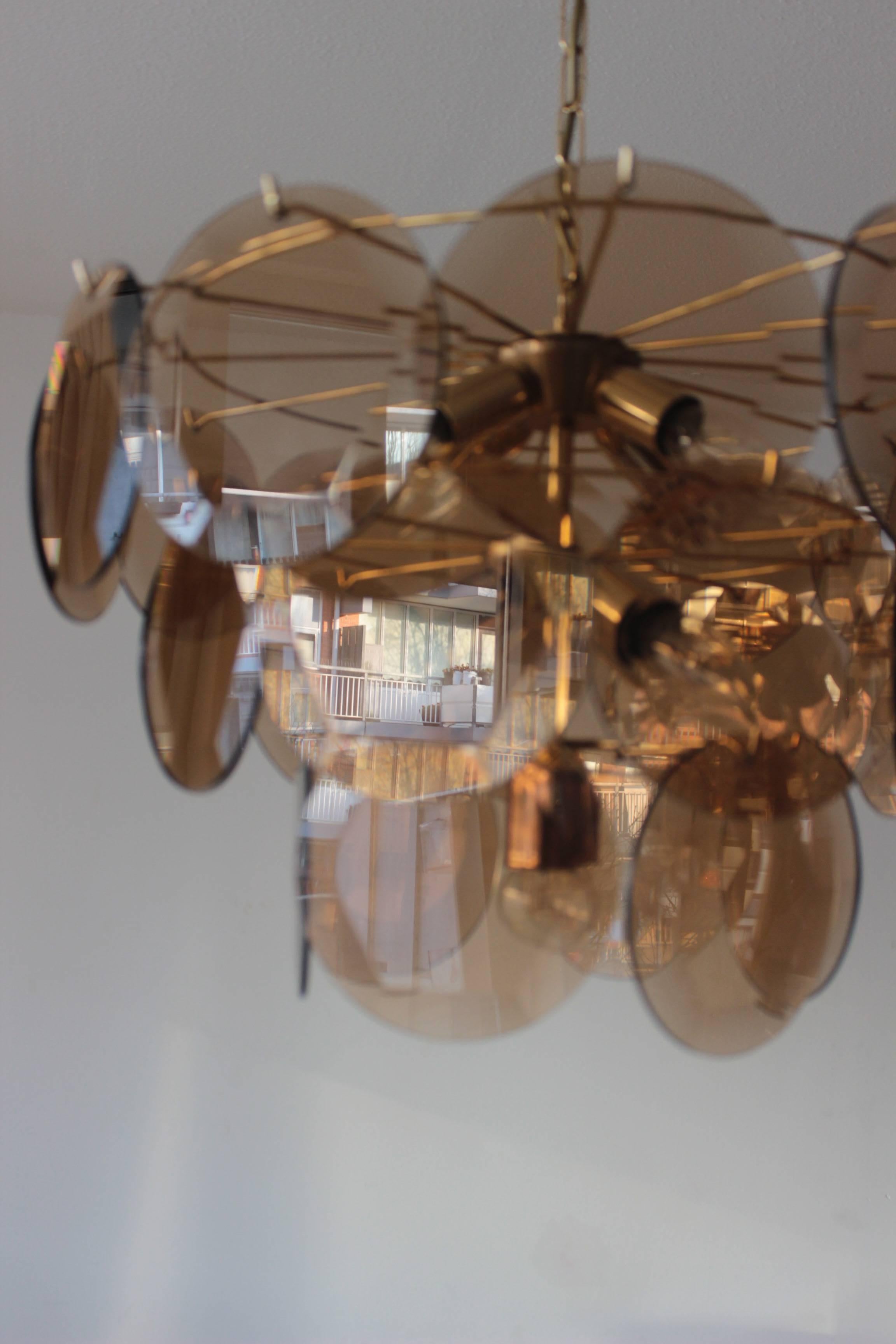 Vistosi smoked glass disc, and brass chandelier from Italy, 1970s.

Beautiful Murano chandelier of style of the Italian designer Gino Vistosi, with large disks, each disk has a diamond shape in the middle and nine lights.
Three layers and 27