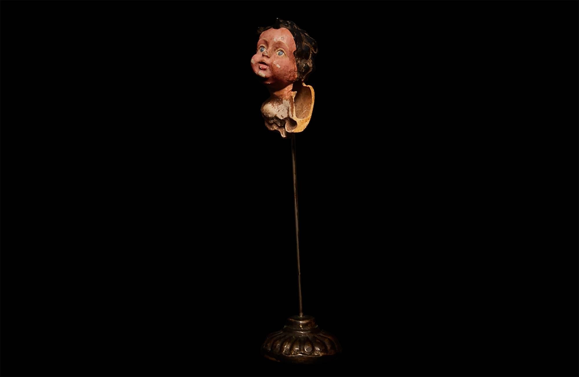 A curious and enigmatic bust of a girl, carved out of bone, hand-painted and worn with time. Mounted on a metal pin with fluted base.