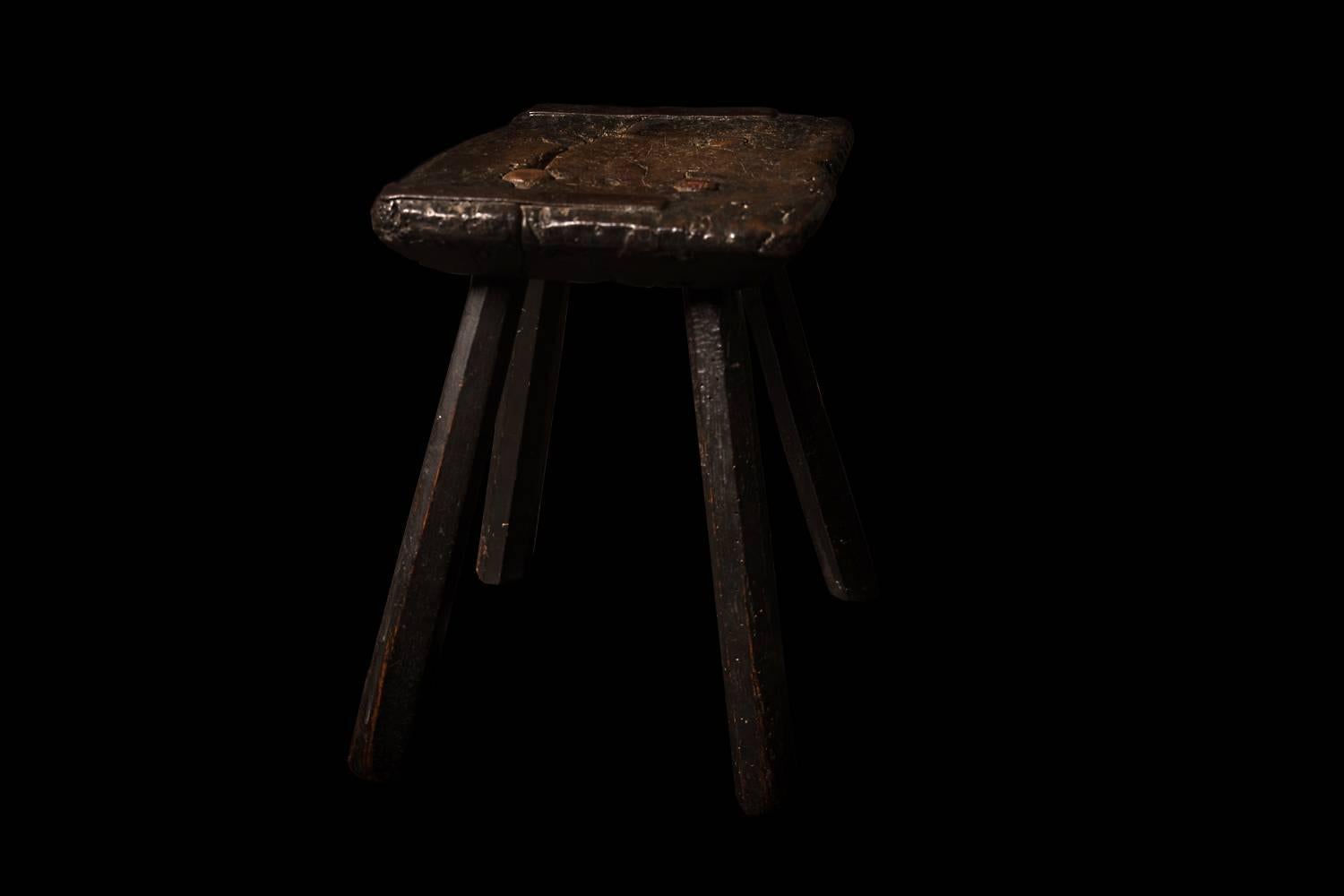 A charming 18th century English Provincial oak stool. The rectangular knarled top raised on four chamfered legs and retaining later village farrier style iron strengthening brackets, most likely a 19th century repair for a family 