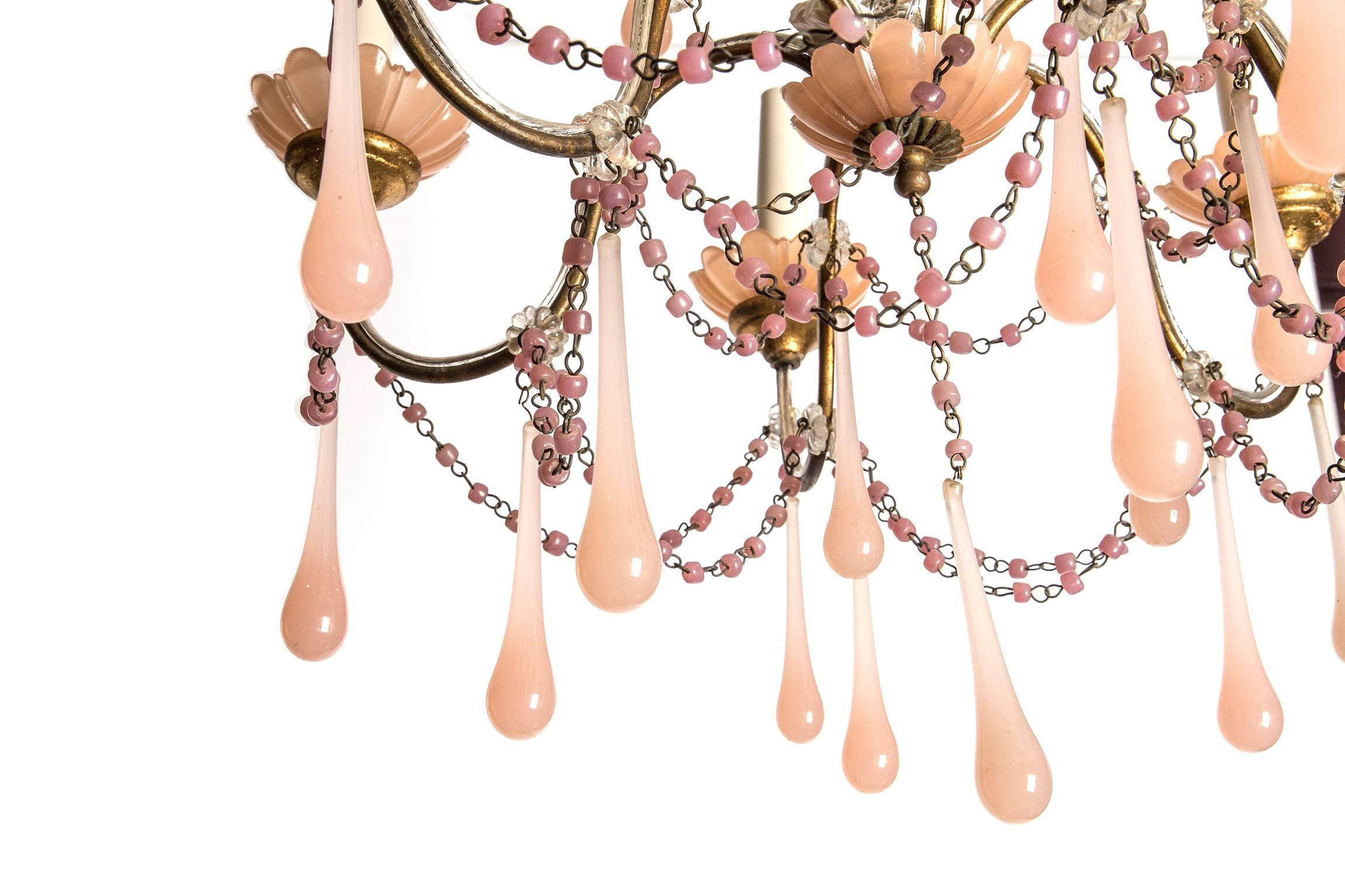 With six elegant tapered candle lights sitting in glass petaled cups, suspended on six undulating branches and featuring three tiers of handblown rose glass droplets. The frame interlaced with delicate glass rose beaded chains. 

A quintessential