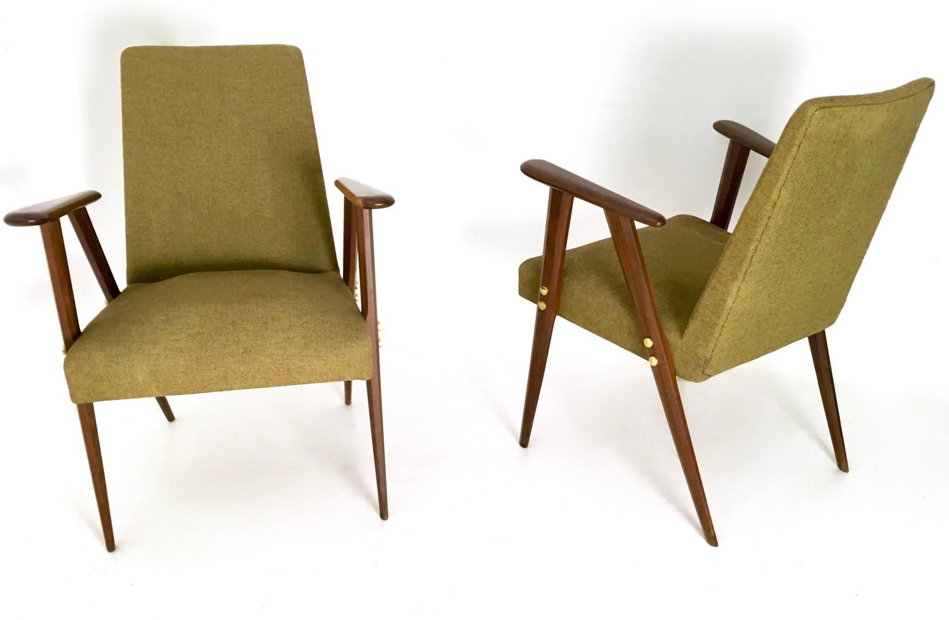 This pair of armchairs features a wooden structure and brass parts. 
The padding is upholstered in fabric. 
In excellent original condition and ready to become a piece in a home.