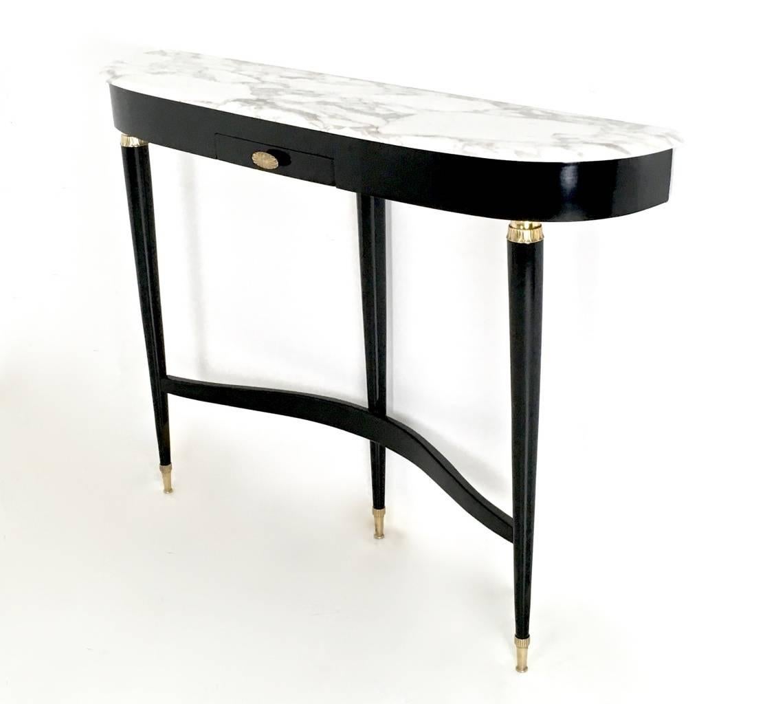 Made in ebonized wood.
It features a white Carrara marble top and brass feet caps.
In perfect original condition and ready to become a piece in a home.

Measures: 
Width 130 cm
Height 93 cm
Depth 30 cm.