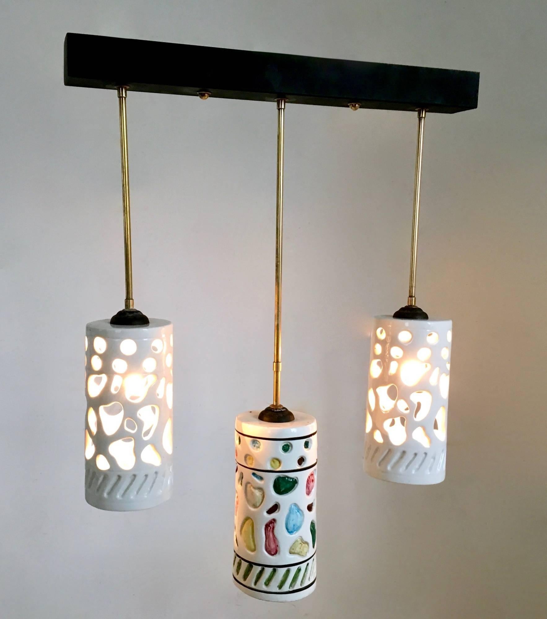Made in Italy, 1960s. 
This chandelier features three white cylindrical ceramic lampshades with colored details and a varnished metal and brass frame.
It is a vintage piece, therefore it might show slight traces of use, but it can be considered as