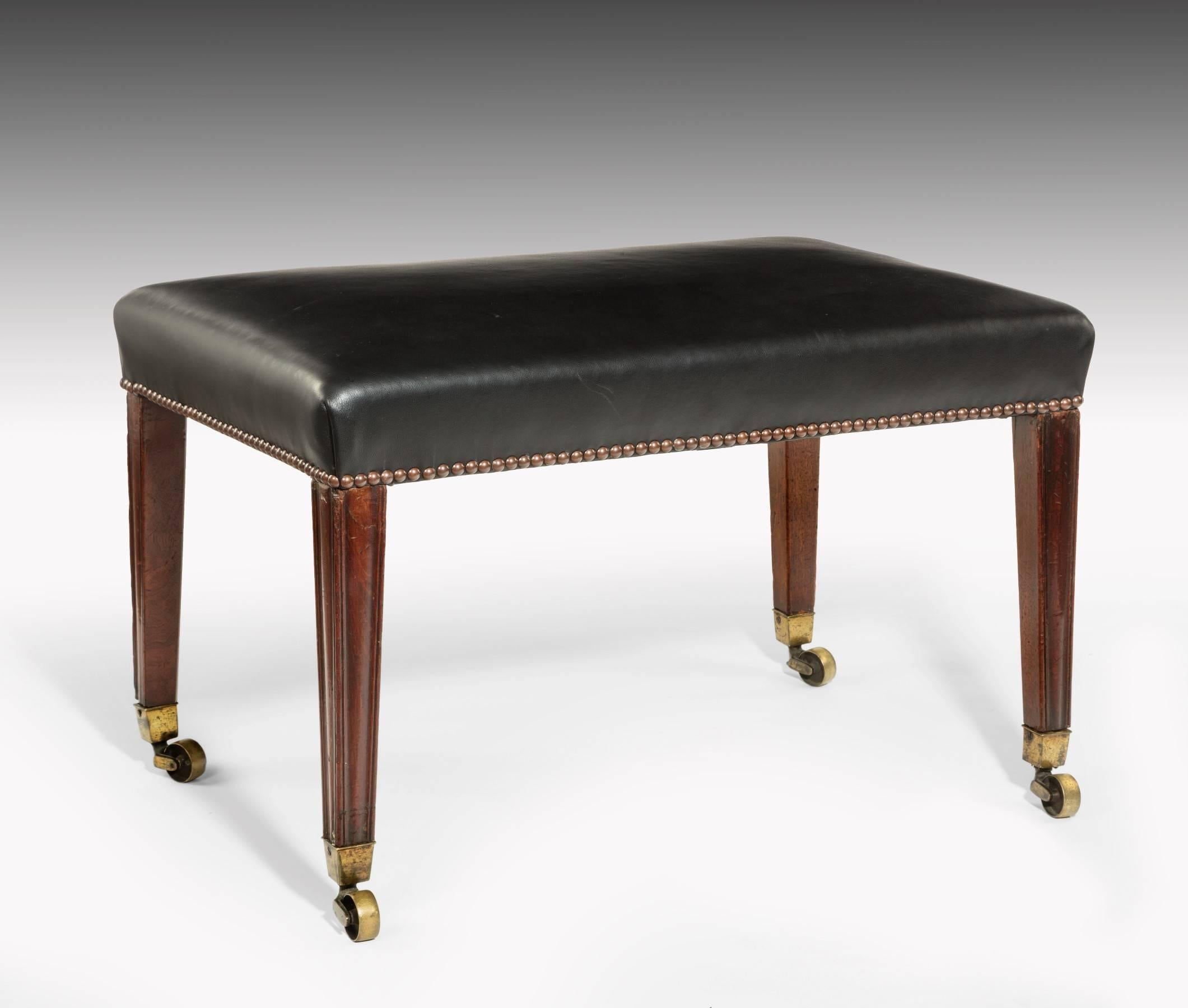 The stool dates from the late 18th century. The square tapering and moulded legs are made from Cuban mahogany and retain their original brass box casters. The stool is upholstered in leather with a stud nail finish and the color and patination of