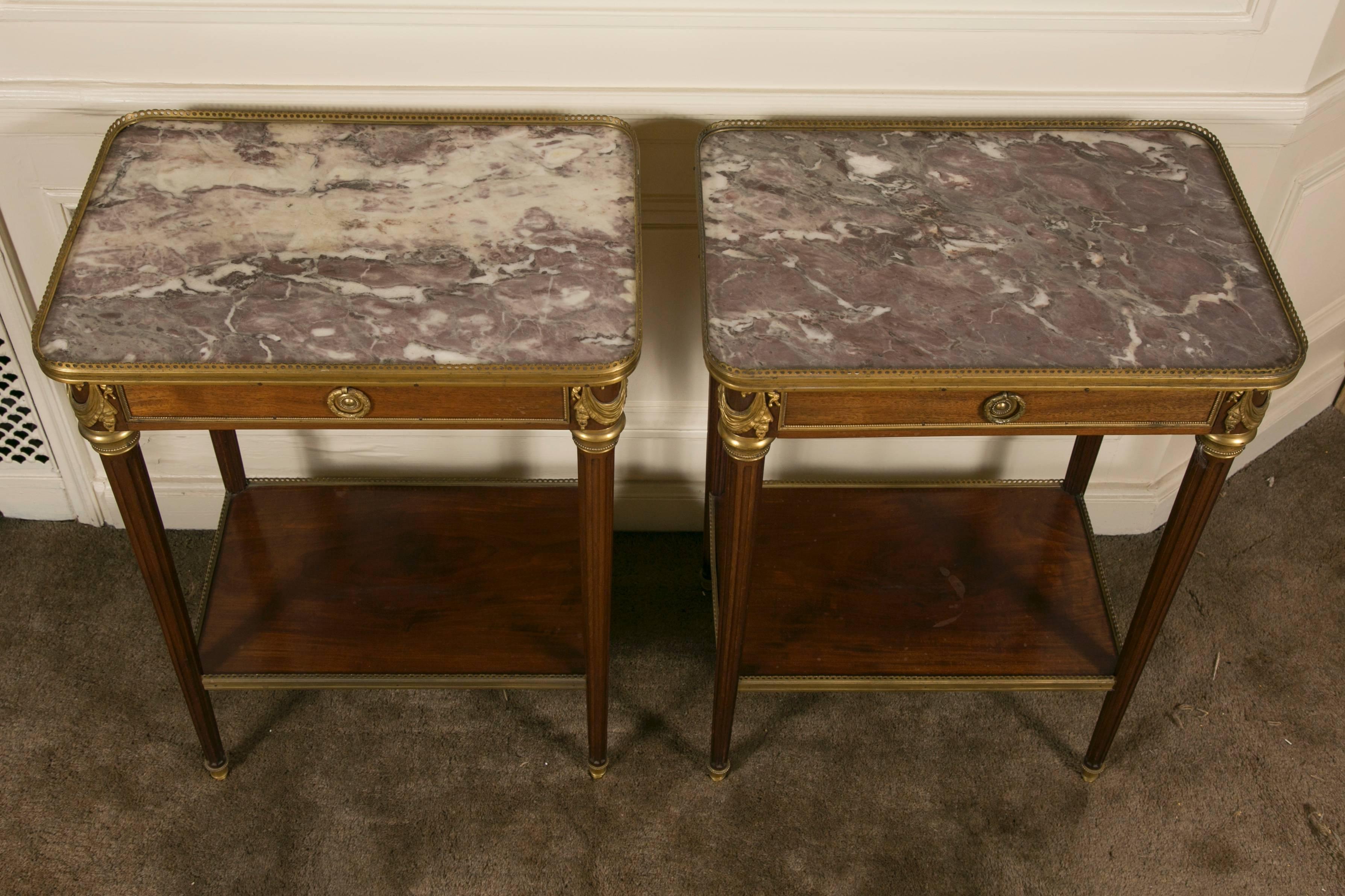 Very fine and elegant pair of French Louis XVI style mahogany side tables on four fluted legs ending with gilt bronze hooves, peach flower marble-top with lower shelf and one drawer. Chiselled gilt bronze trim around the marble-top and shelf. In the