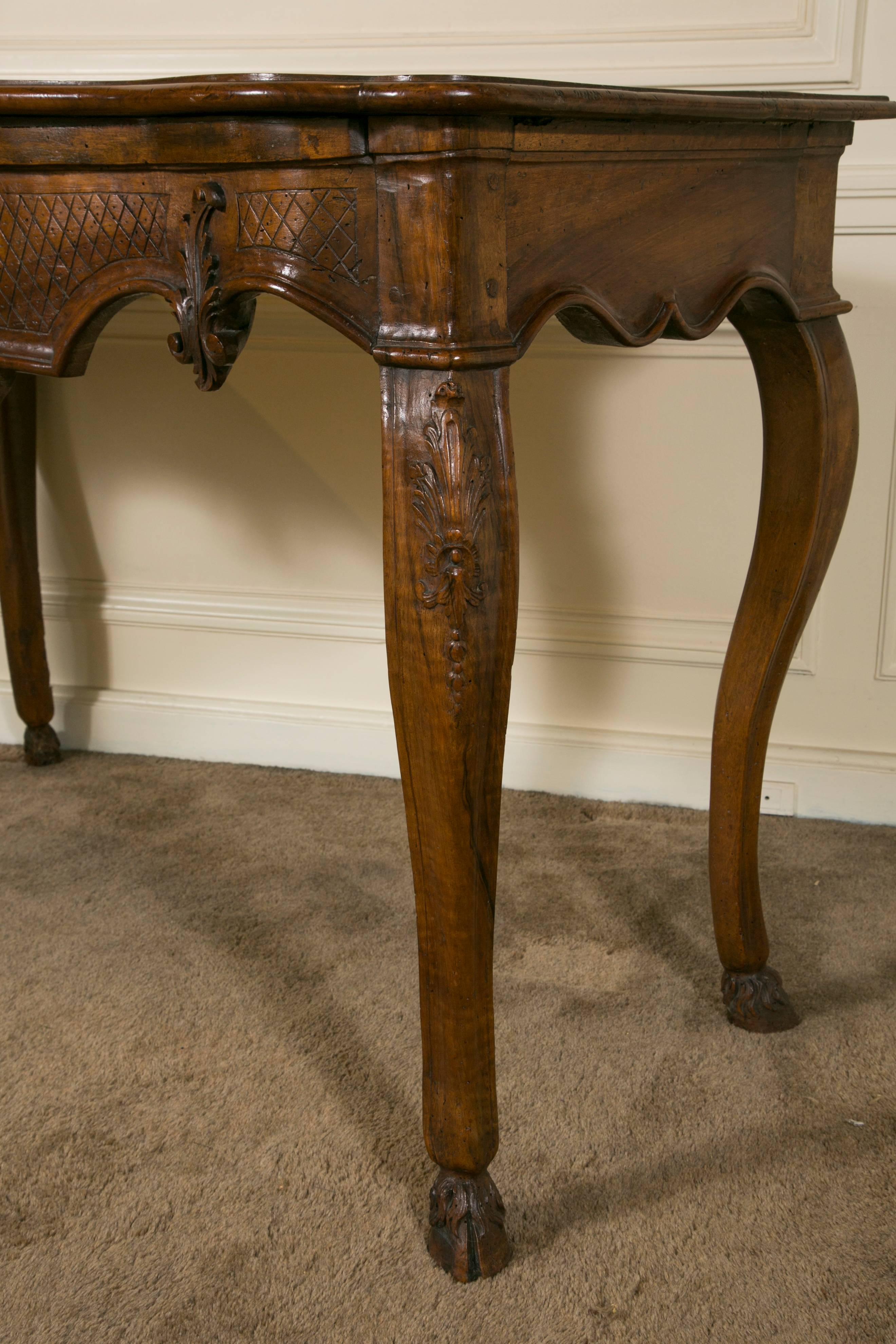 18th century beautifully and finely carved French Avignon Provence walnut wall or sofa console table with wooden top. The serpentine apron is centered with a carved large Regence shell and with a carved leaf on each side.
The four cabrioles legs