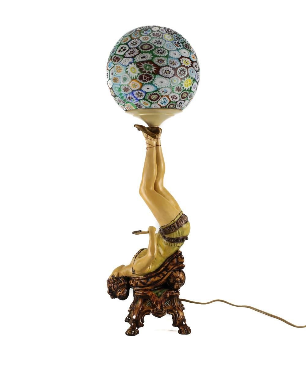 An attractive polychrome decorated cast metal lamp taking the form of a 1920s burlesque entertainer. The young beauty portrayed with bobbed hair, beaded waistband, fan and ankle laced flats as she balances the colorful glass shade, constructed in