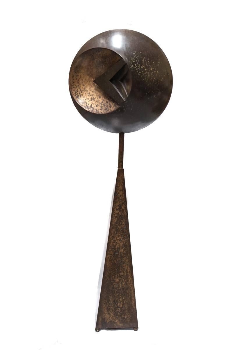 An imposing floor standing bronze sculpture, the round disc of concave form with adjacent protruding geometric triangular elements, attached to an elongated neck, tapered from a square base resting on four balled feet. Distressed and eroding effects