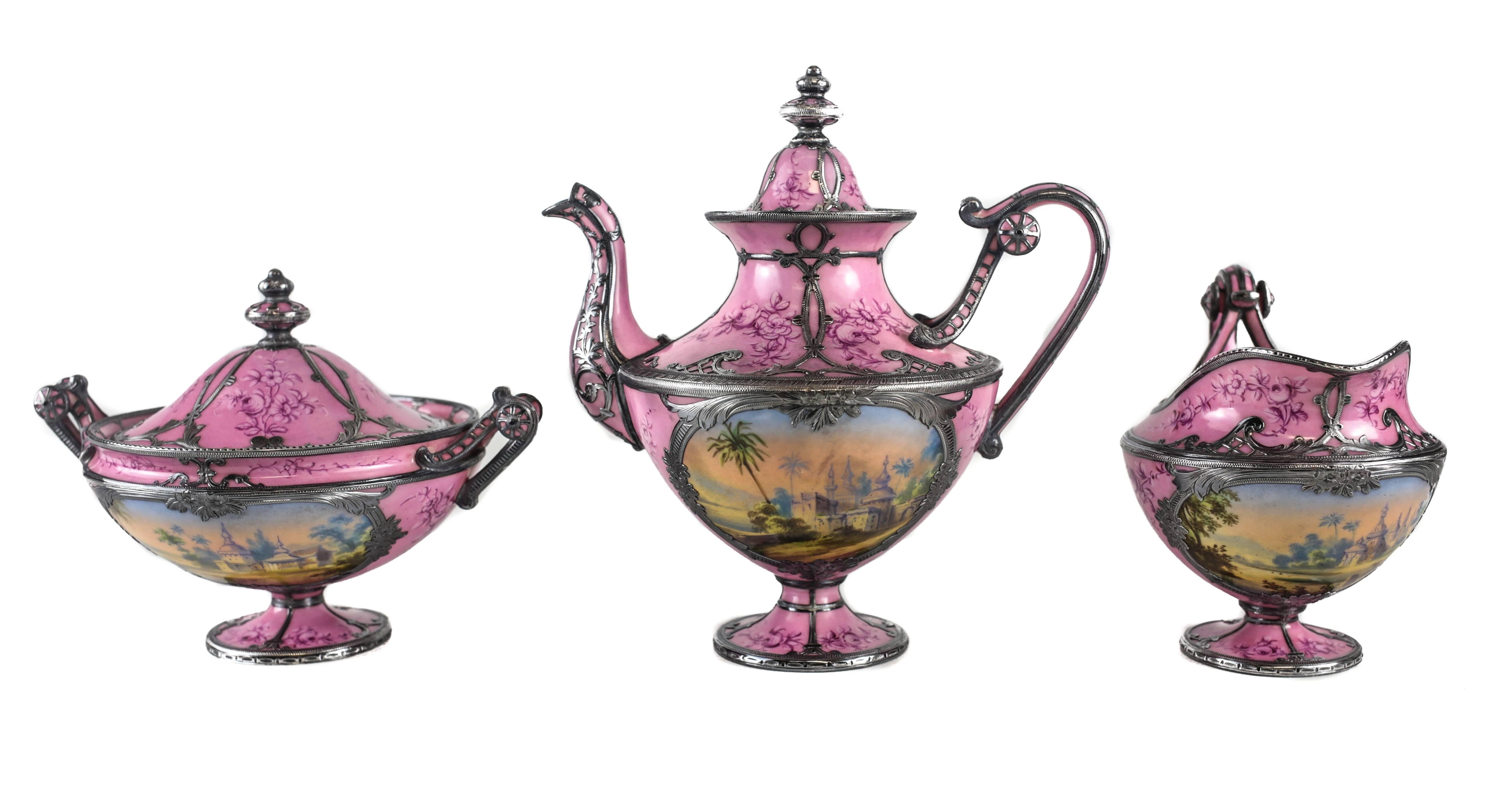 An exceptional French porcelain tête-à-tête (tea service for two) in the Sevres style with a rose pink ground and the finest hand etched silver overlay. The hand-painted topographical scenes depict a royal Arabian oasis with lush greens and a