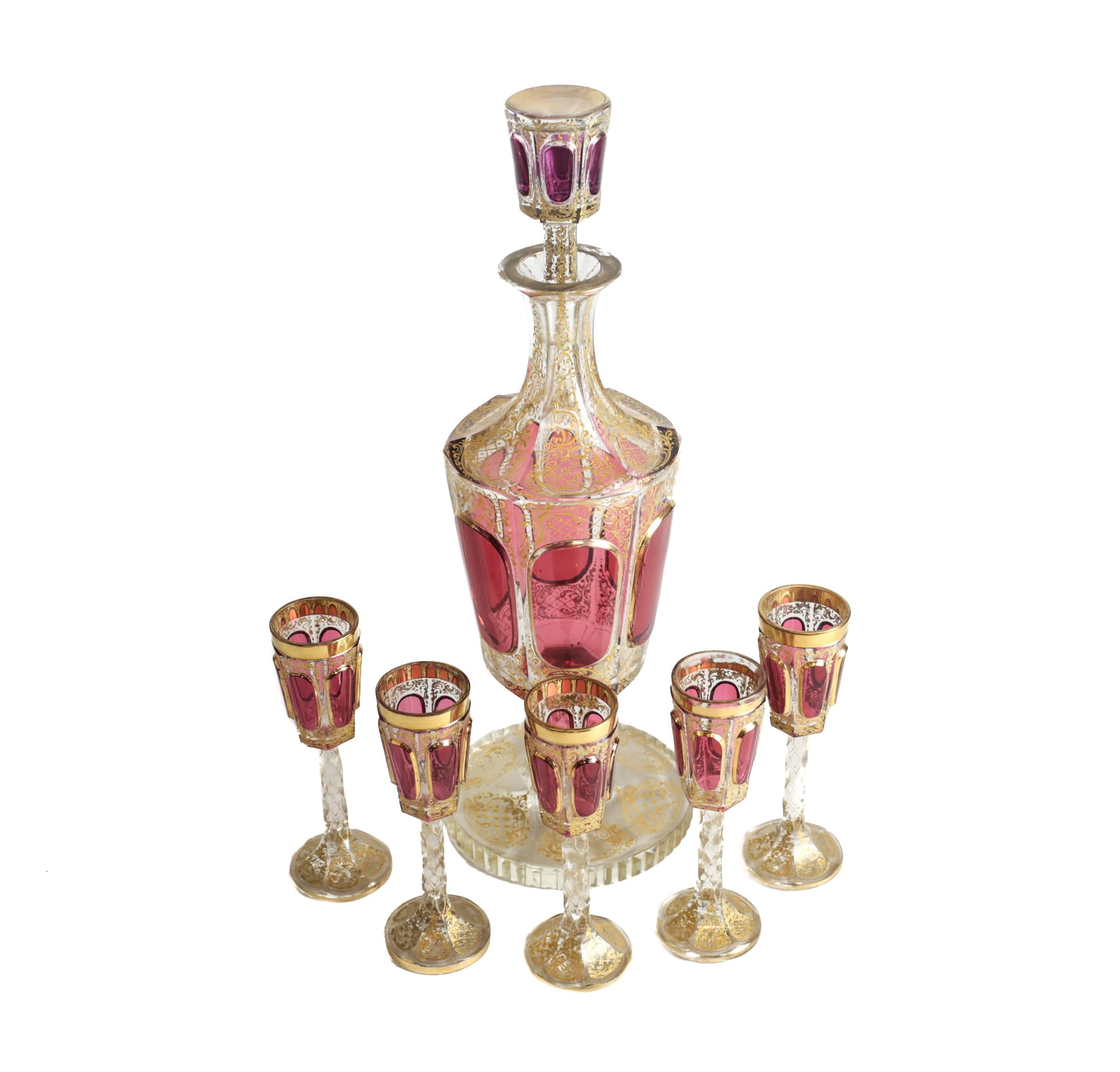 A striking liquor service with glass cut in two layers, cranberry red and clear, each with richly applied thick gilt decorations. The stems of the cordial glasses with angle cut prisms complimenting the stem of the decanter. A fine quality example