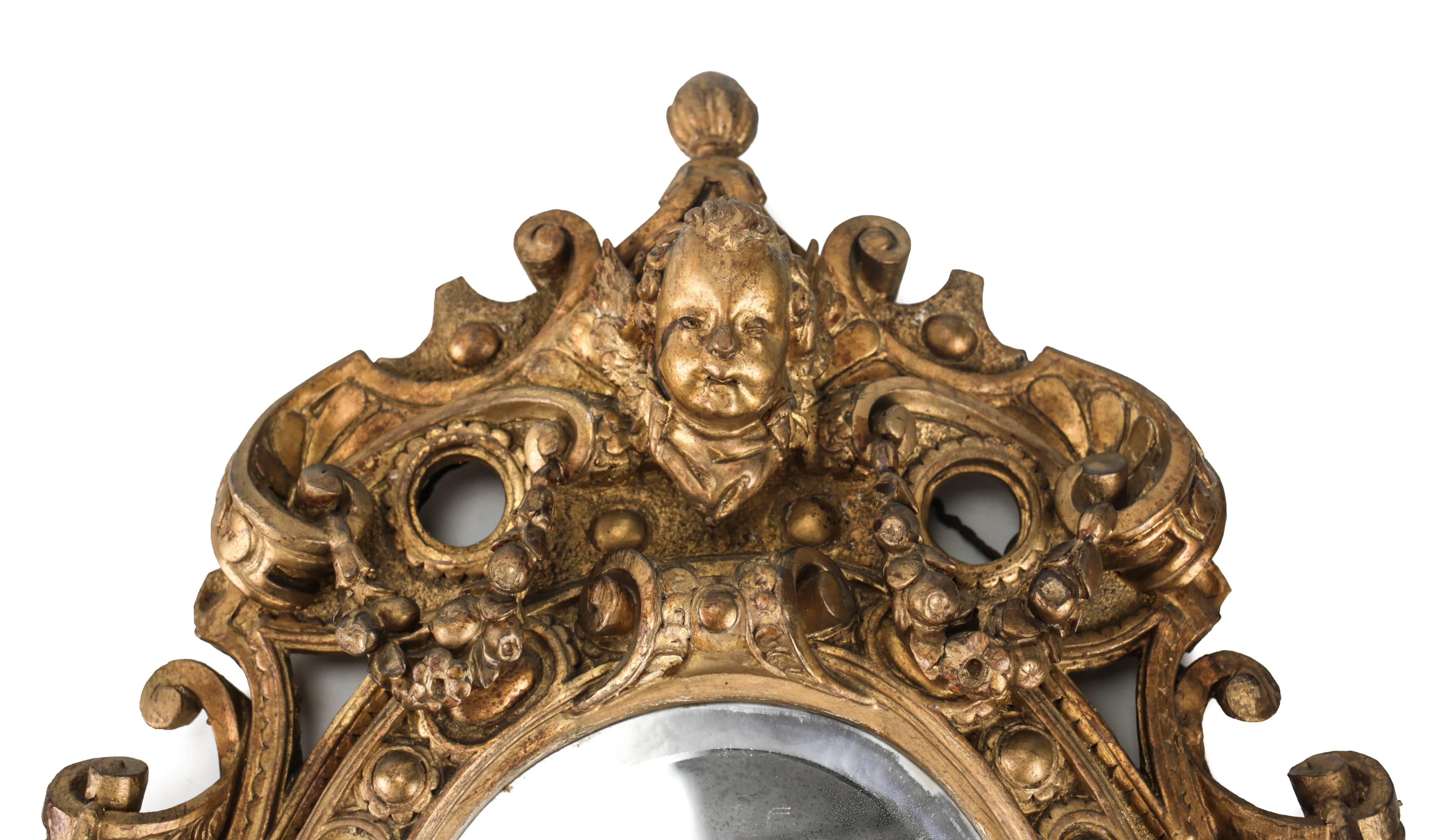 An attractive pair of oval giltwood mirrors from the late 18th century, each hand-carved with an intricate decoration of floral swags, ribbons and open work, the head of a winged cherub stationed atop each.

Previously purchased from Christie's in