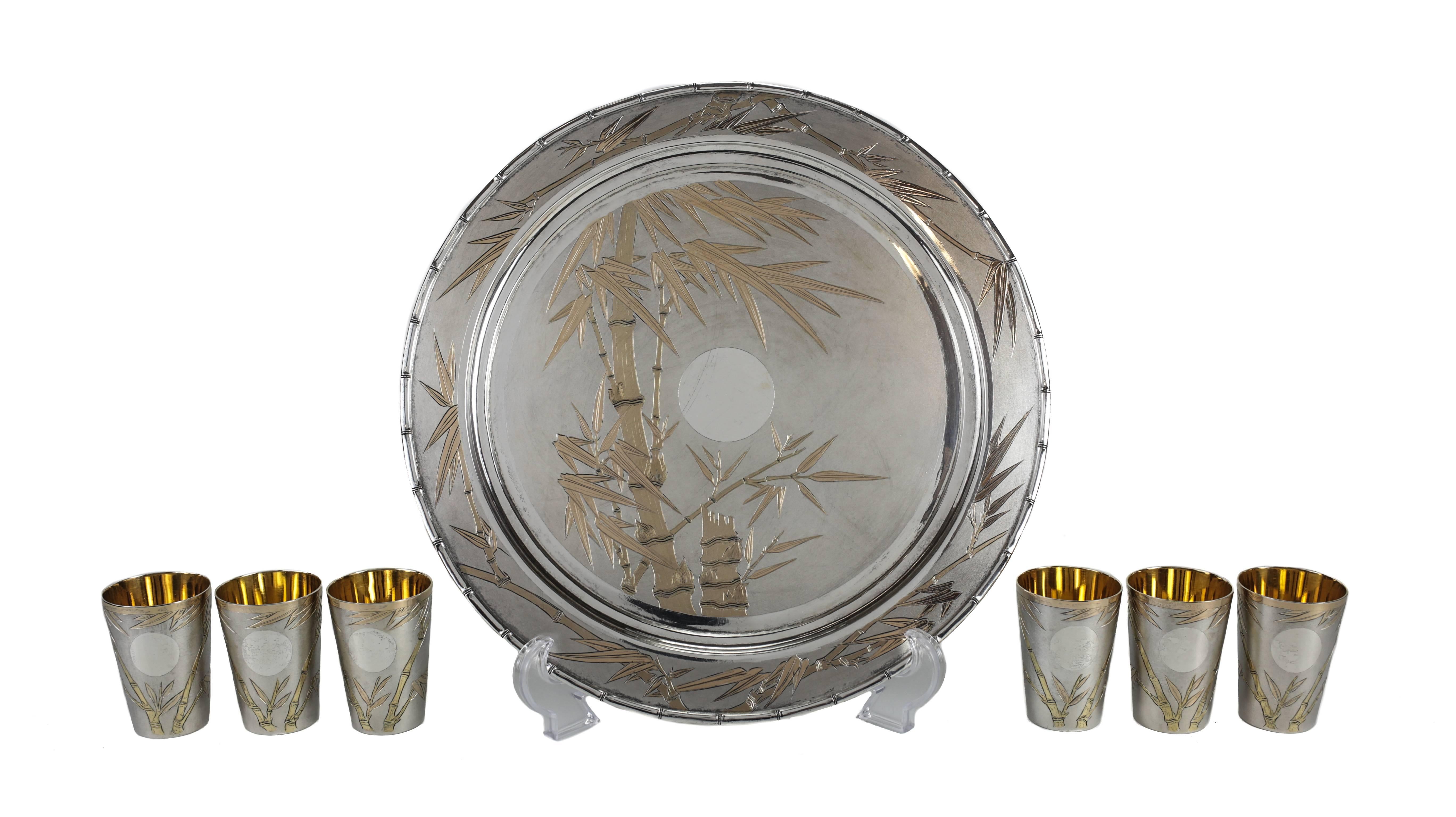 A Mid-Century decorative sake service from Japan consisting of a serving tray and six sake cups (shot glasses). The tray with a hand engraved night scene depicting a bamboo tree and moon, the border further engraved with a matching bamboo leaf