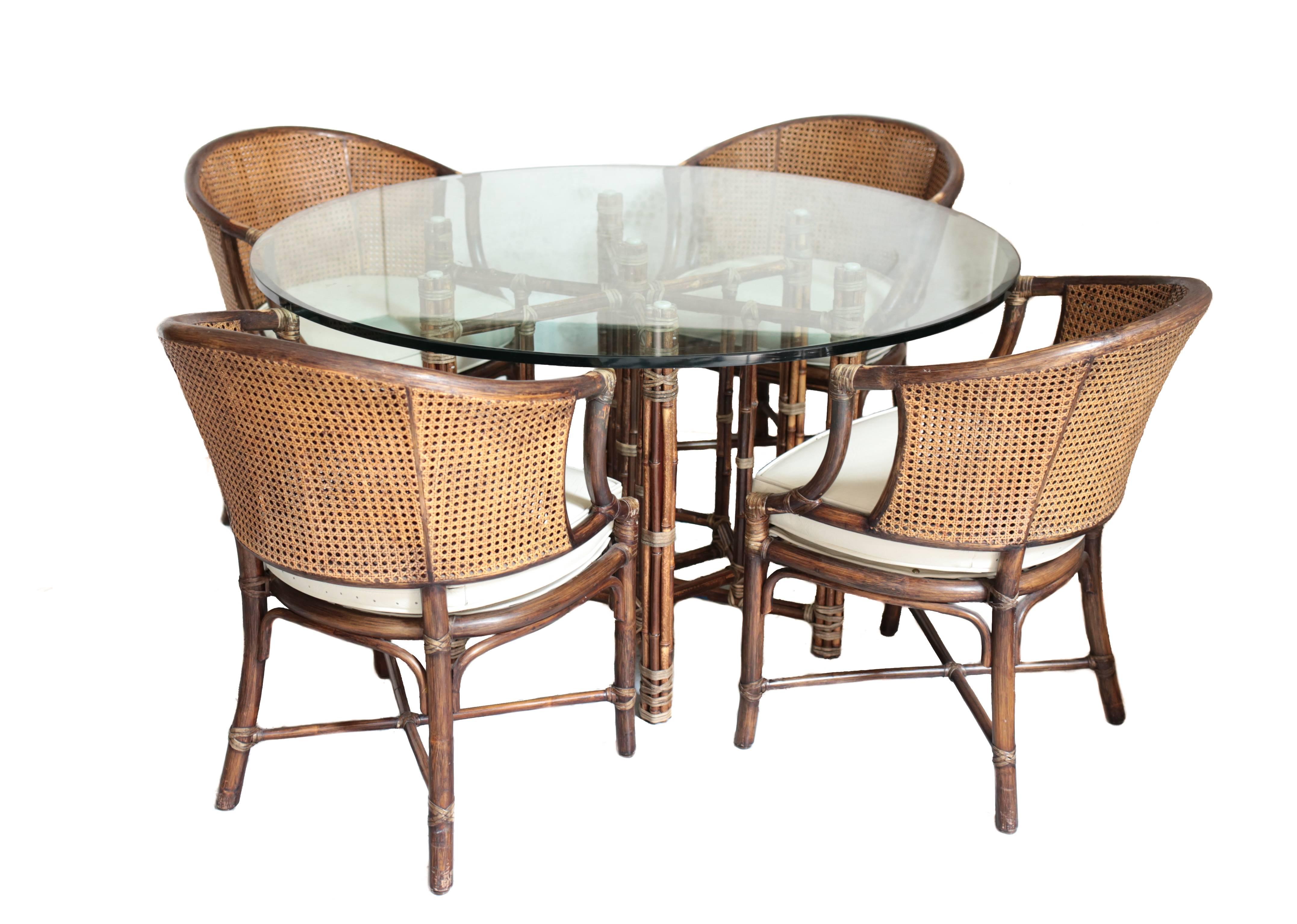 A stunning vintage bamboo and rattan dinner and chair set by McGuire. Comprised of a beautiful bamboo table with a large and thick circular glass panel tabletop. Four rattan backed chairs with white leather cushions, circa 1970.

Measures: The glass