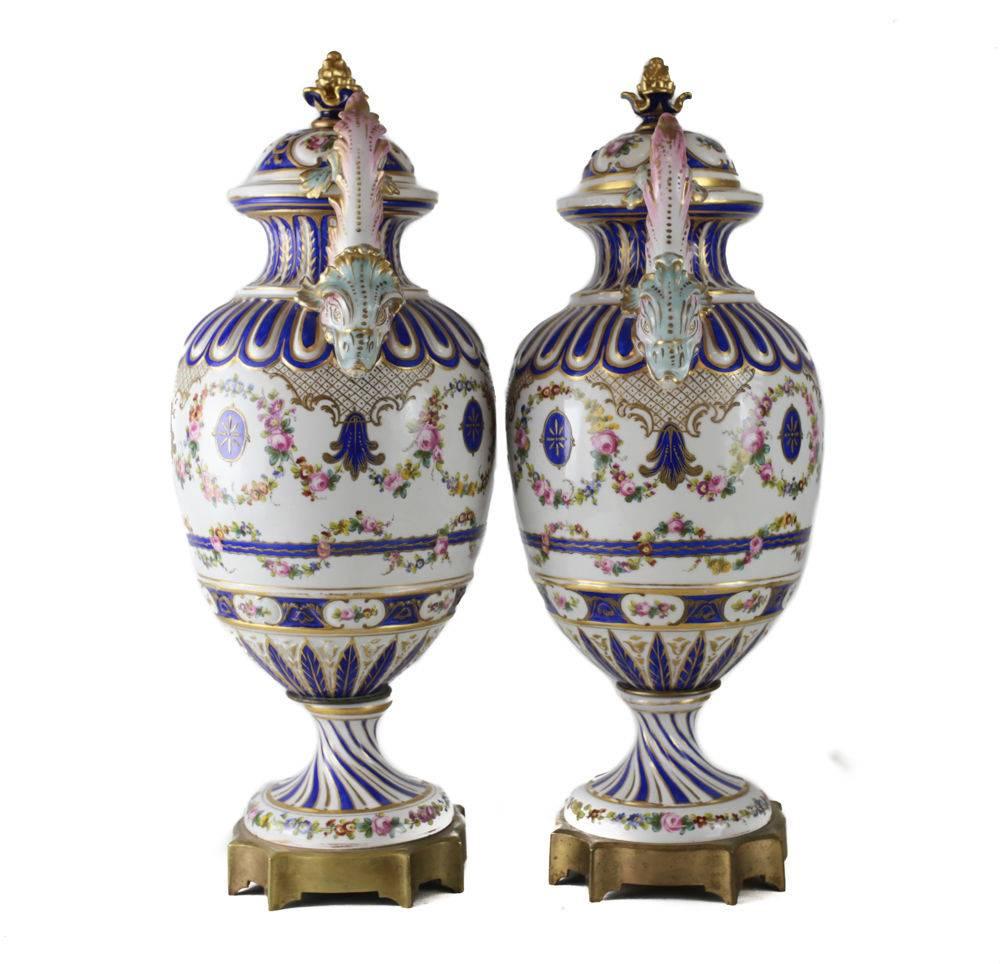 A fine pair of large 19th century Sevres France porcelain hand-painted urns. Beautiful hand-painted florals in a swag design with cobalt blue ground and gilt accents. Double dolphin form figural handles. Mounted to a gilt bronze base, both signed