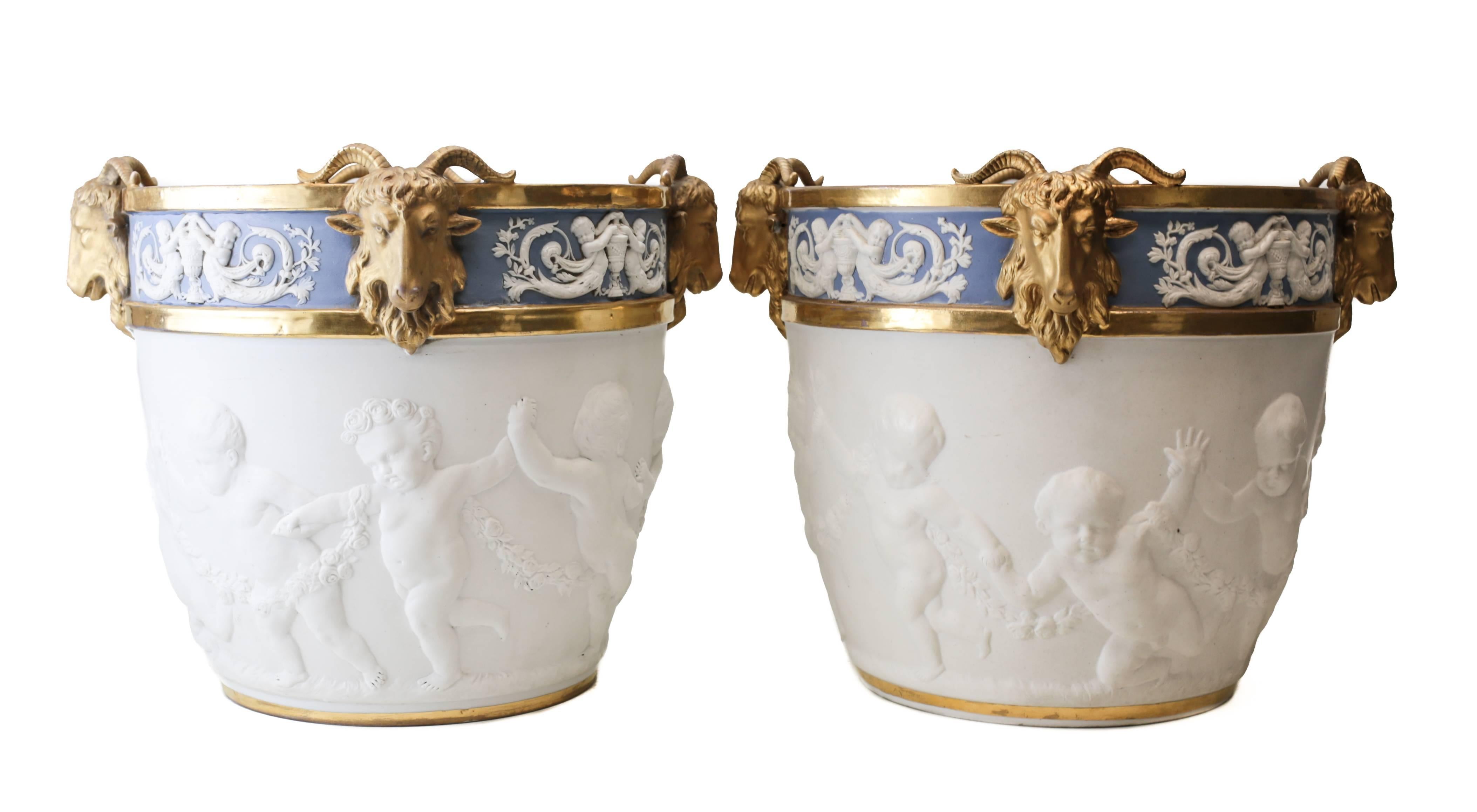 A large and attractive matching pair of cache pots from Sevres of the late 19th century. Charming hand chased cherubs holding hands while frolicking on the bisque central finish. The top rim of the cache pot has more cherubs with four applied gilt
