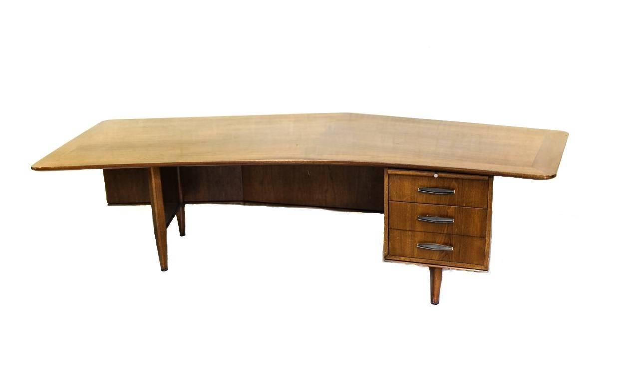 A large Mid-Century walnut executive desk by Monteverdi Young. Off-center peaked front in the boomerang style, inlaid wood trim and three compartment drawers with slant angled handles. Original paper label inside top drawer.