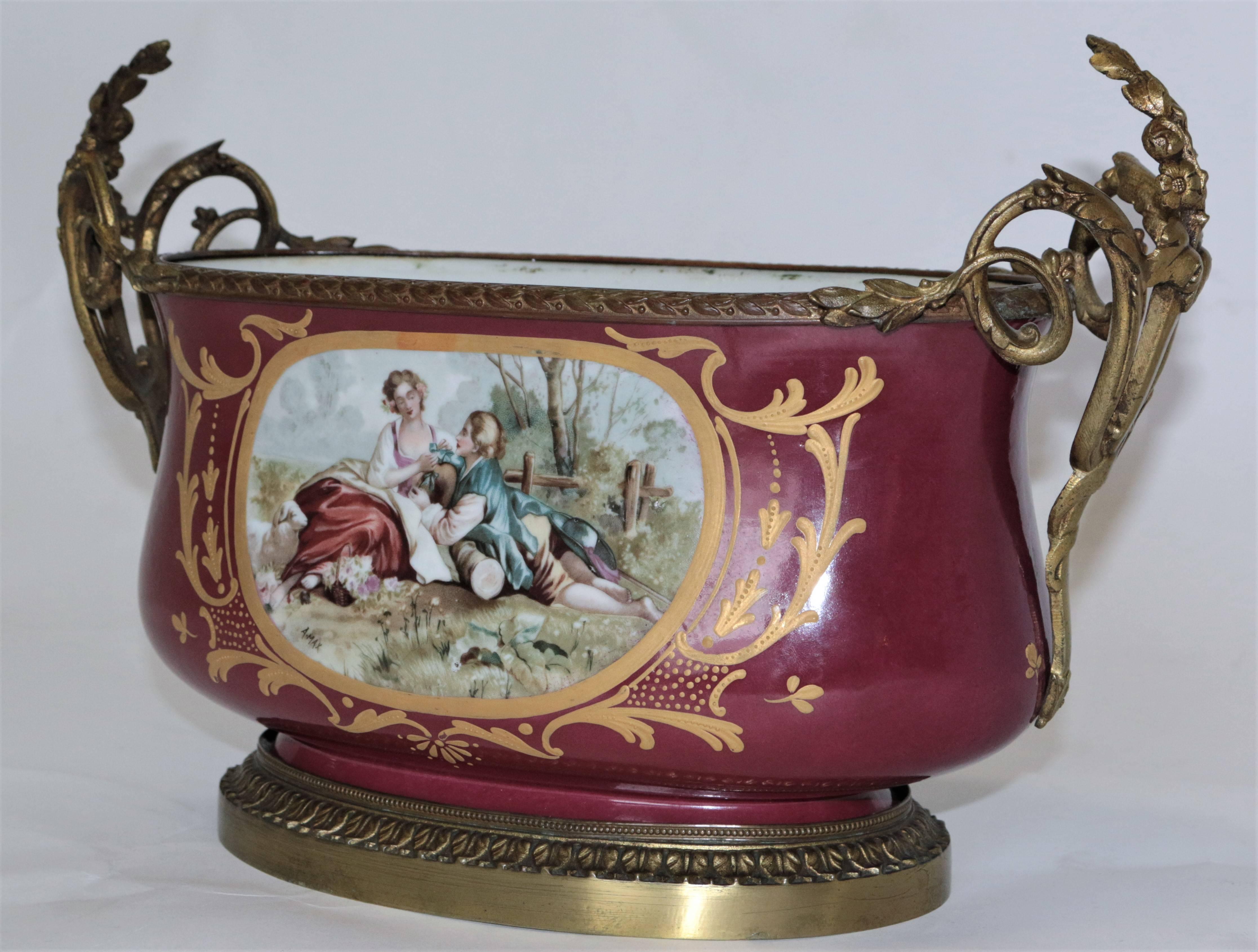 This amazing hand-painted center piece is in pristine condition. The portrait on the sevres depicts a picnic love scene. The bronze floral handles extend upward and overlap the lip. Throughout the entire piece detailed precision is shown.