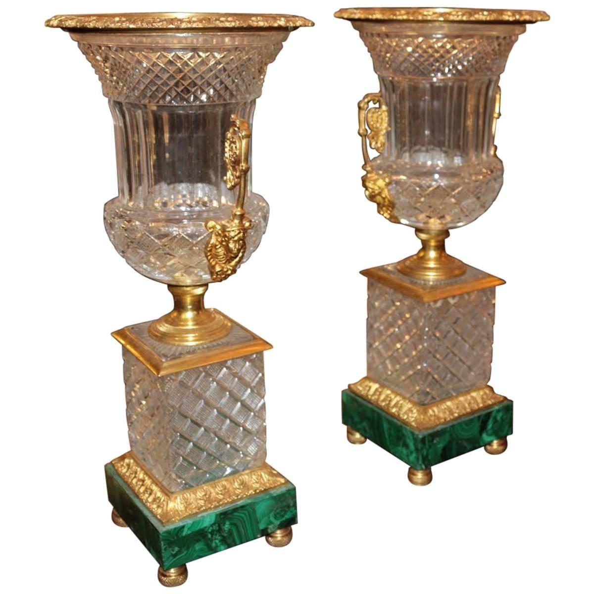 These stunning cut crystal urns are mounted on ornate bronze with dark green malachite bases. Their neoclassical styling and sumptuous details would make for incredible mantel ornaments. Raised on malachite base. Sold in a set of two.
