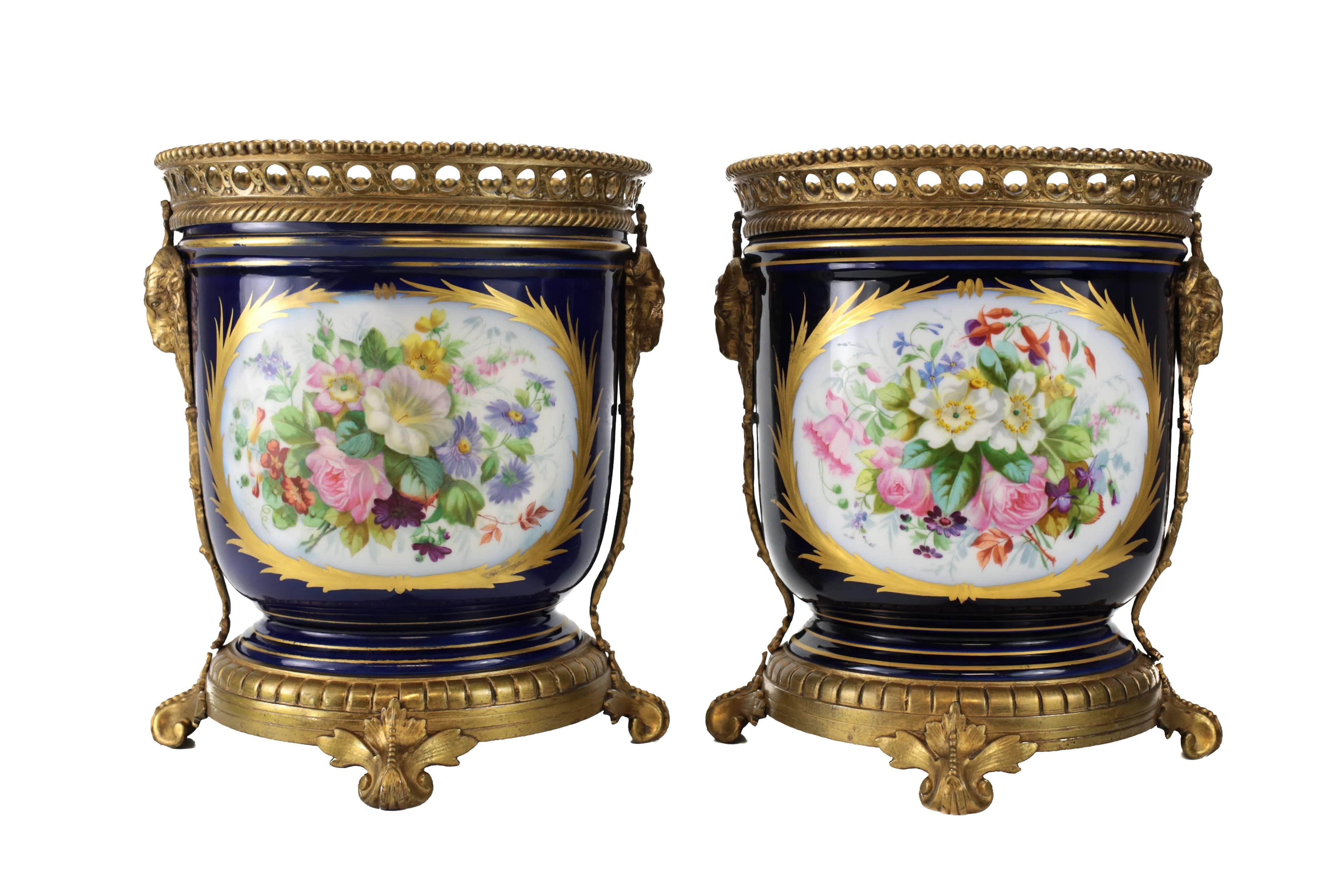 A matching pair of late 19th century French porcelain and gold decorated bronze cache pots. Hand-painted courting scenes to each, with an elaborate floral bouquet to the reverse. Bronze-mounted base with four acanthus formed feet, reticulated rim
