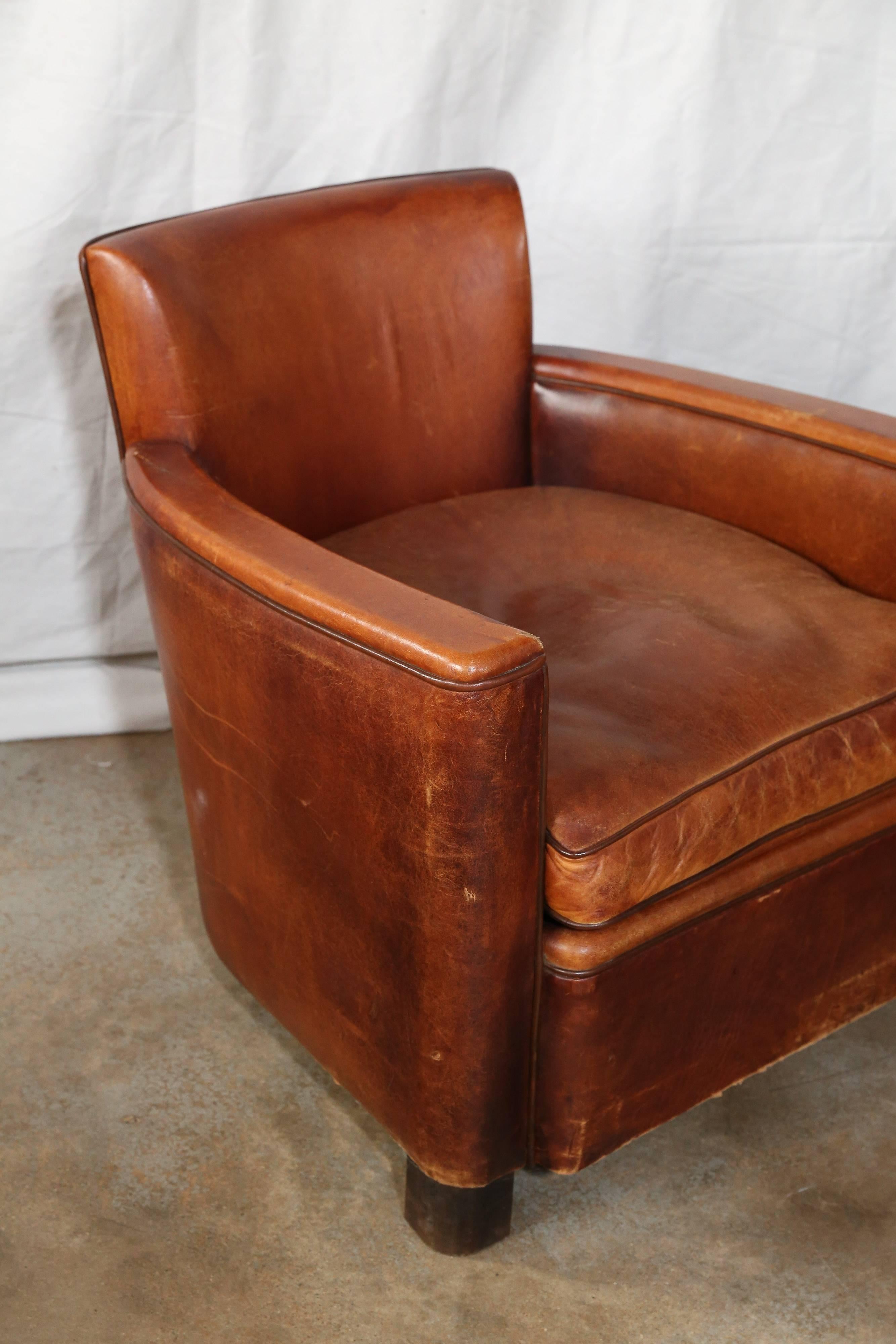 From France, leather club chairs in original cognac tone leather. Piped in a darker shade and finished with brass nailheads on back. With a Mid-Century look and chunky dark wood feet, the small-scale of these chairs adds to their appeal.
