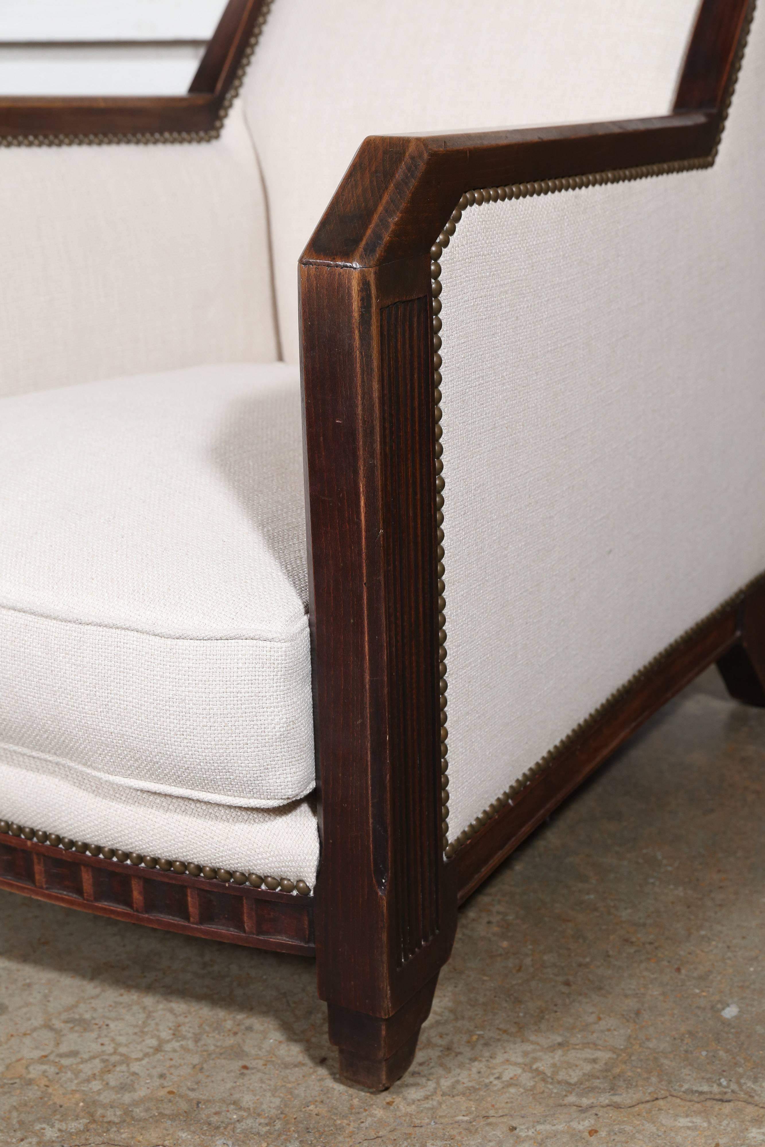 Newly upholstered in an off-white linen blend with brass nailheads, this stunning pair of Art Deco chairs in walnut exhibit the Cubist influence with their bold geometric lines. Unique and theatrical.