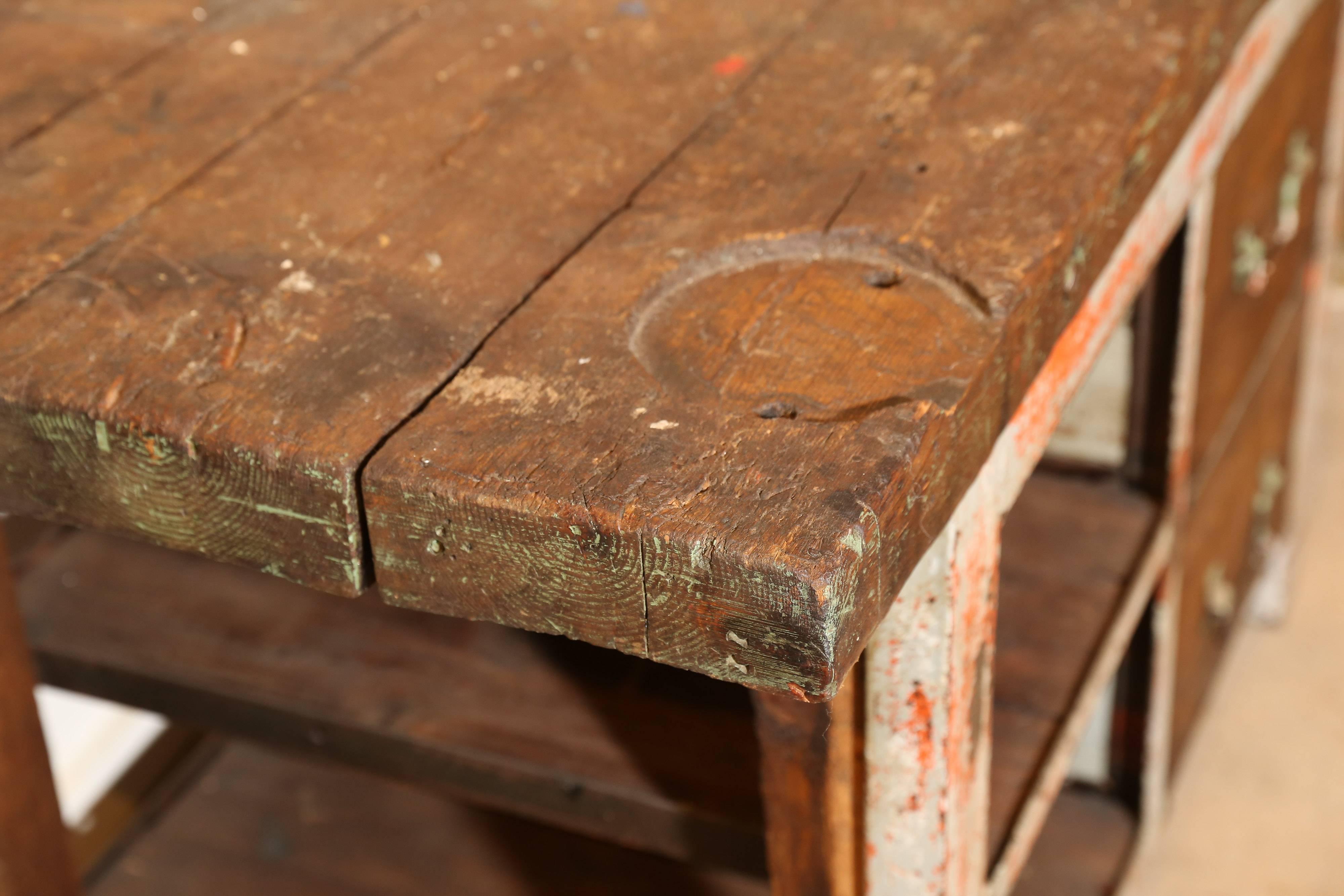 Solid as a rock and a real workhorse, this rustic work table from France tells its own story. A heavy metal frame supports a dense solid wood top. With chipped and worn grey and red paint, a space notched out for a vice, wooden shelves and two deep