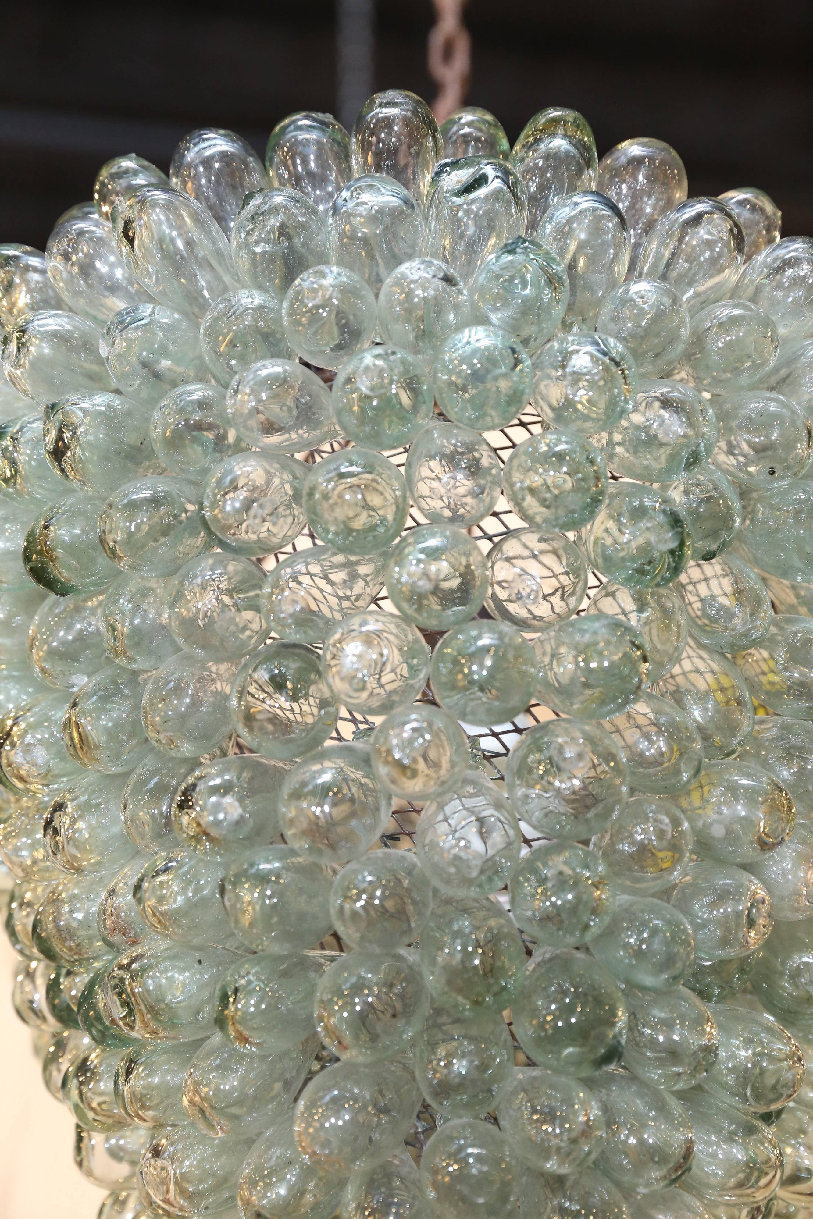Dozens and dozens of pale green blown glass bubbles, each approximately 1.5 inches in diameter, cluster together to form an enchanting heavenly object that adapts itself to a myriad of styles. With each bubble individually attached to a sturdy mesh