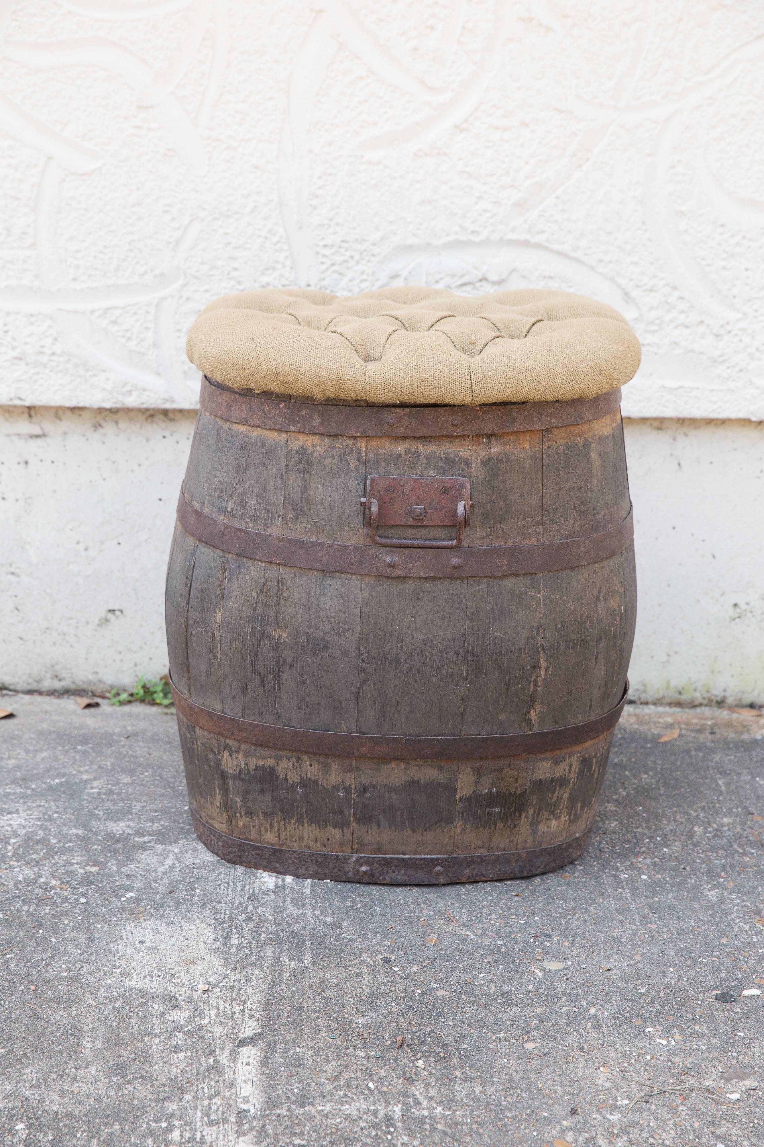 An old oak whiskey barrel from France has been re-purposed into a handy stool with the addition of a hinged lid covered with tufted burlap. The name E.Roulleau can be seen on the side of the barrel. Extra seating / extra storage.