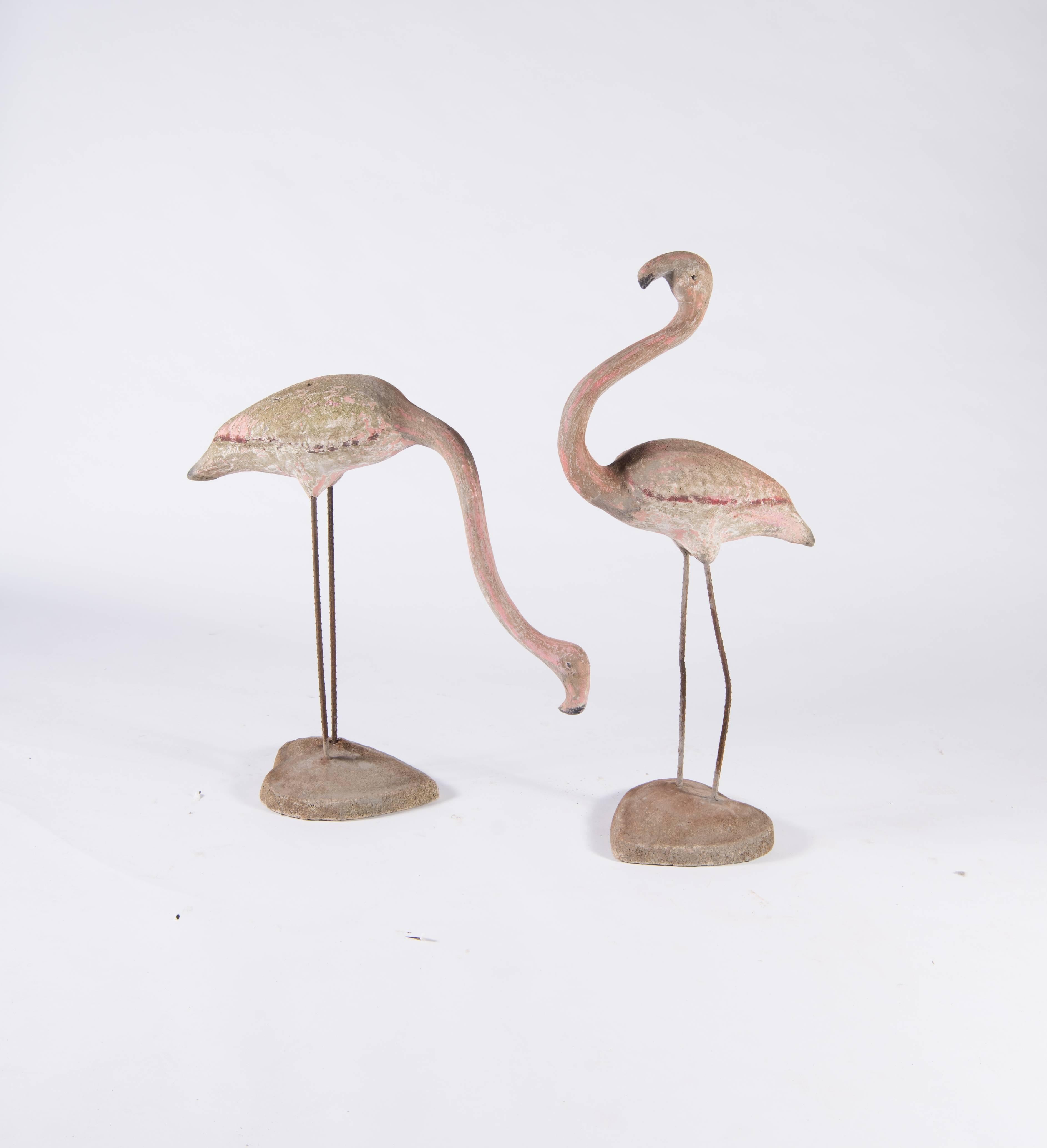 A very special pair of concrete flamingos. Heavy and sturdy, the concrete birds Stand solidly on legs made of rebar sunk into a hefty concrete base and retain traces of the original paint which has been worn and dulled by age into a soft pink